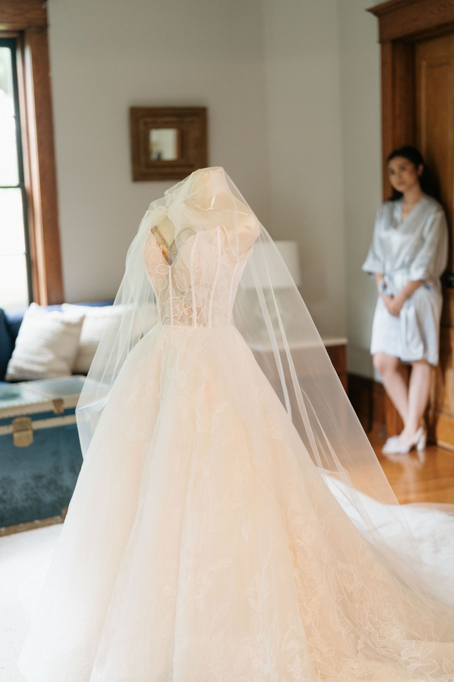 Wedding dress with delicate tulle veil displayed in natural light against hardwood floors and white walls.