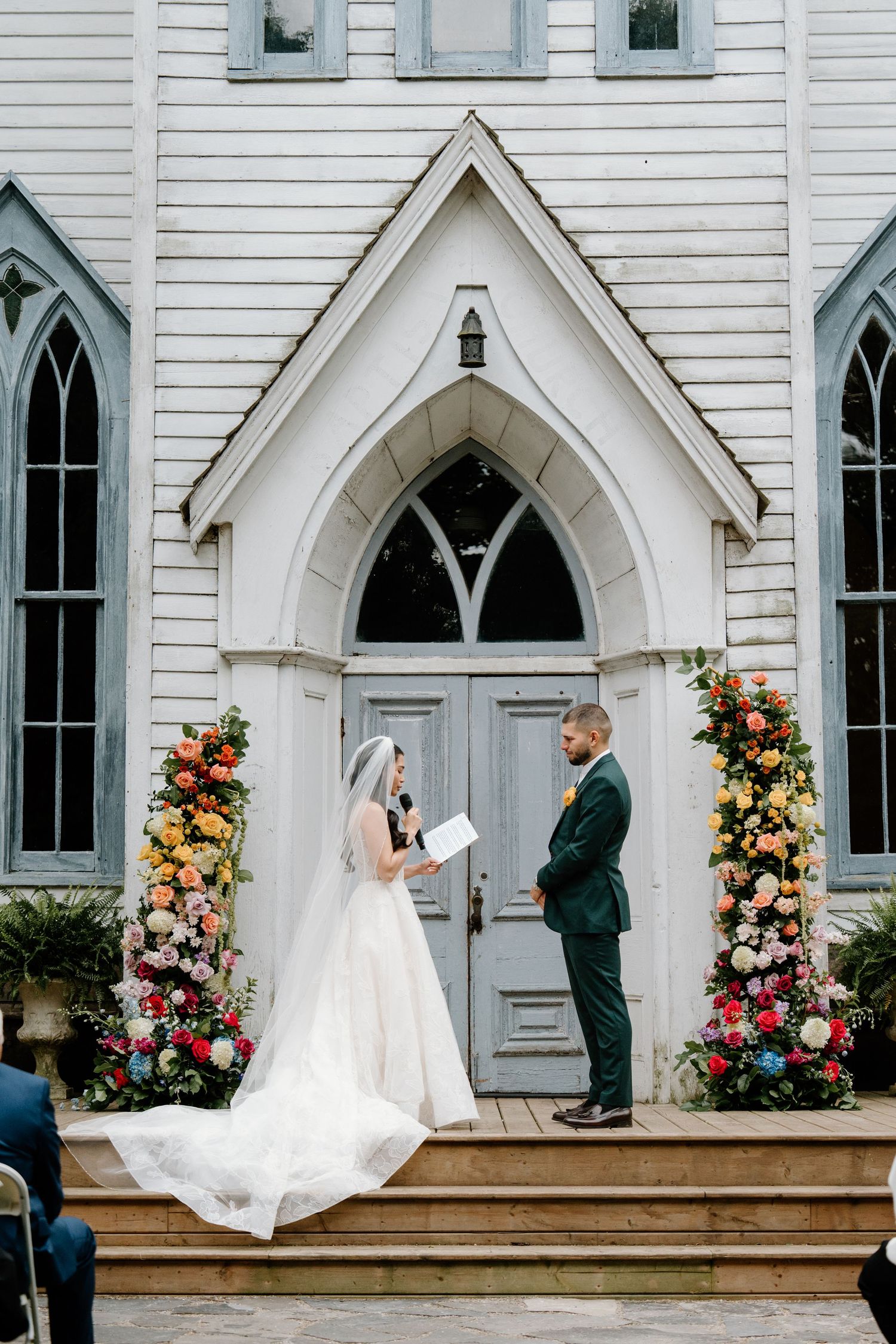 A wedding ceremony takes place at a charming white Gothic-style church with arched windows and floral decorations.