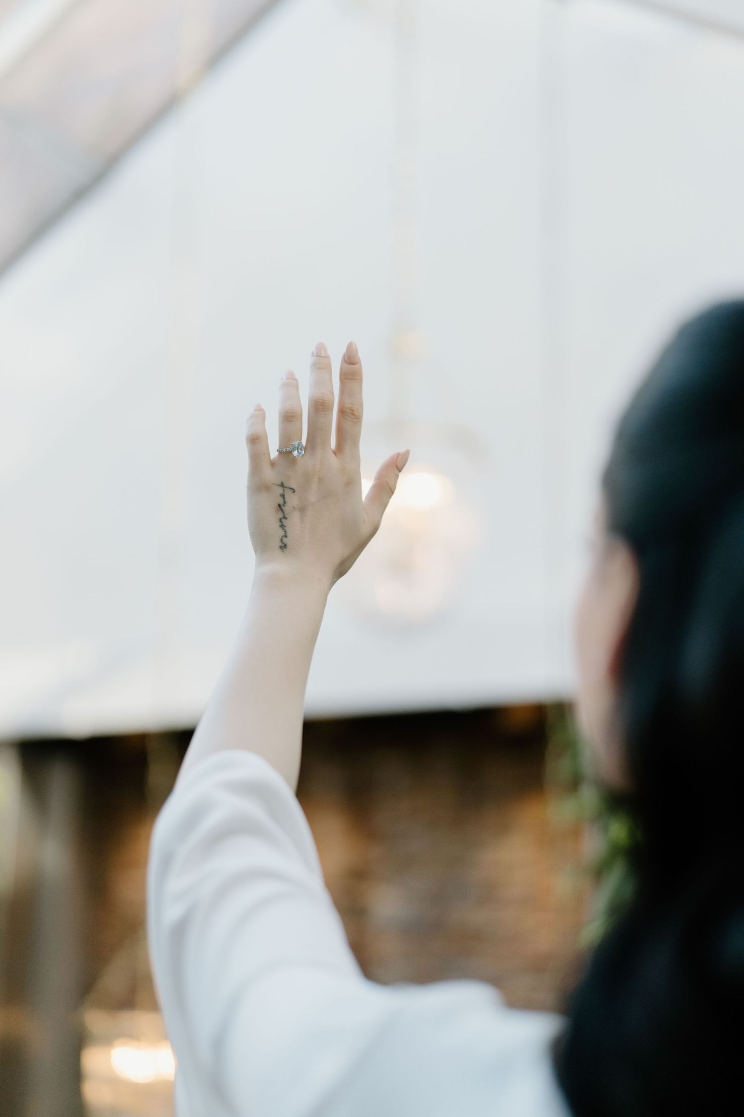 A person raises their hand in worship during a church service with soft lighting and blurred background.