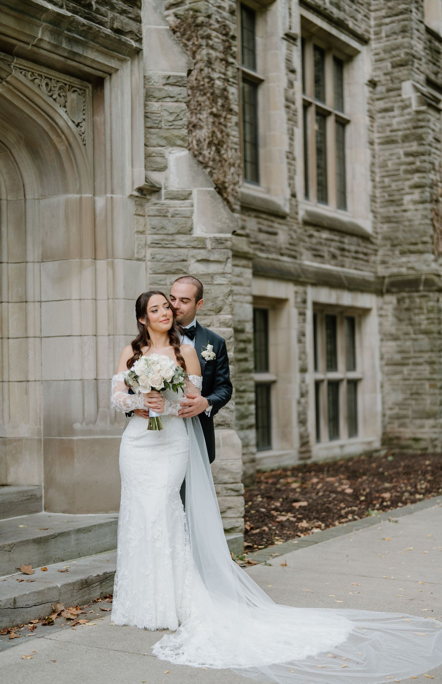 A bride and groom share an intimate moment against a stone building's exterior wall during their wedding photoshoot.