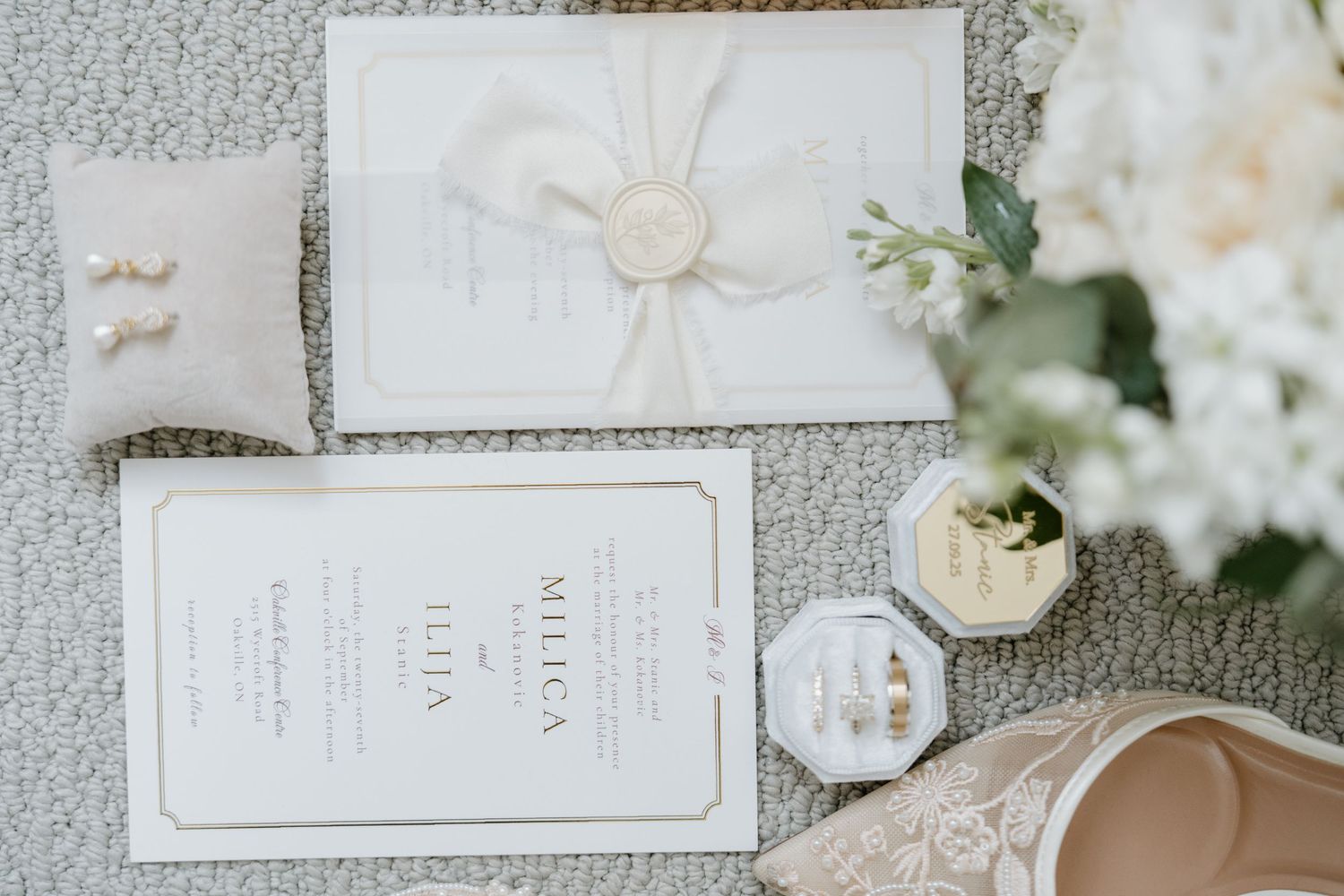 Wedding invitation suite with white floral details and elegant calligraphy laid out on textured gray background.