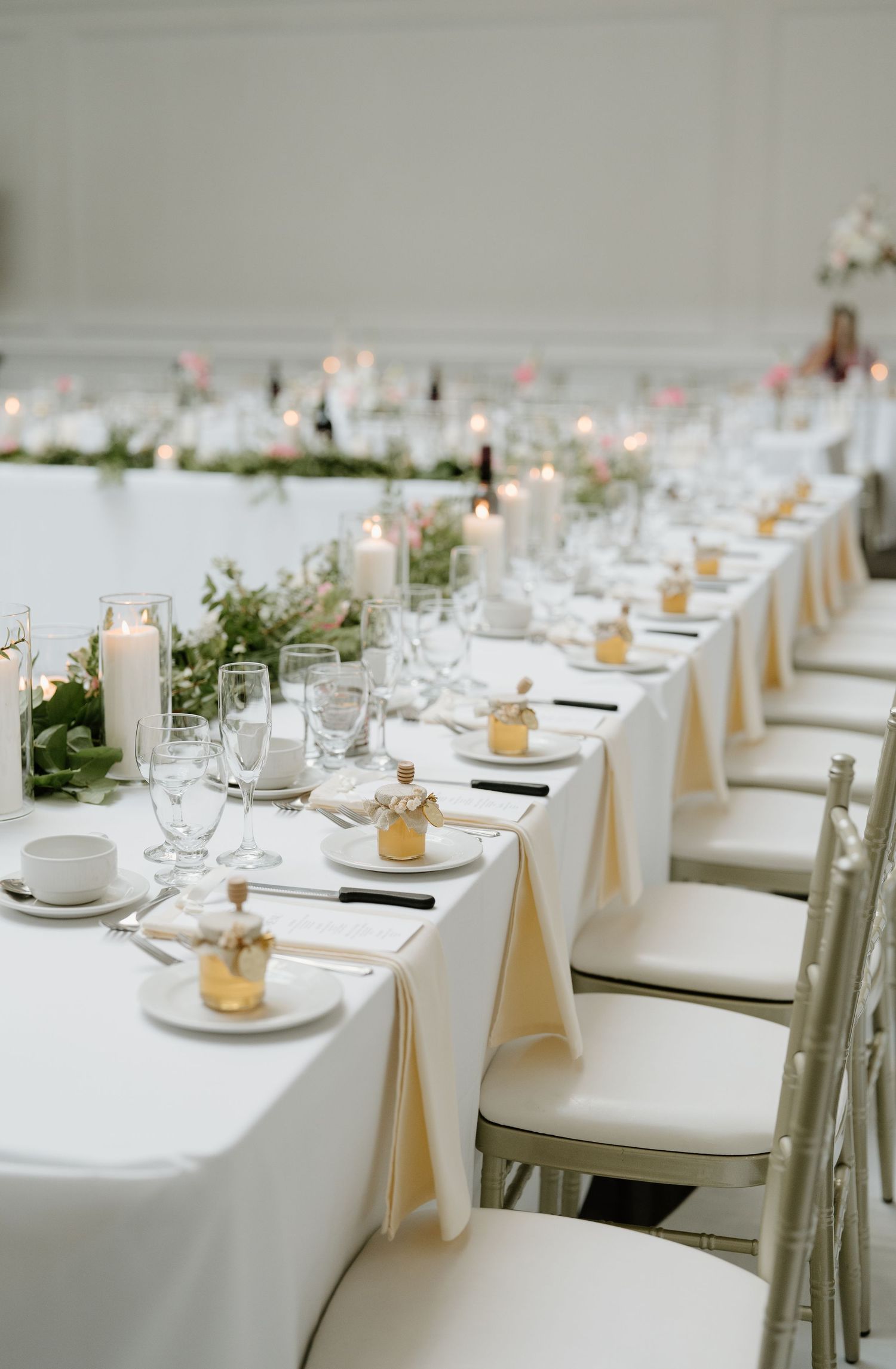 Elegant wedding reception tables set with white linens, candles, and place settings in a minimalist style.