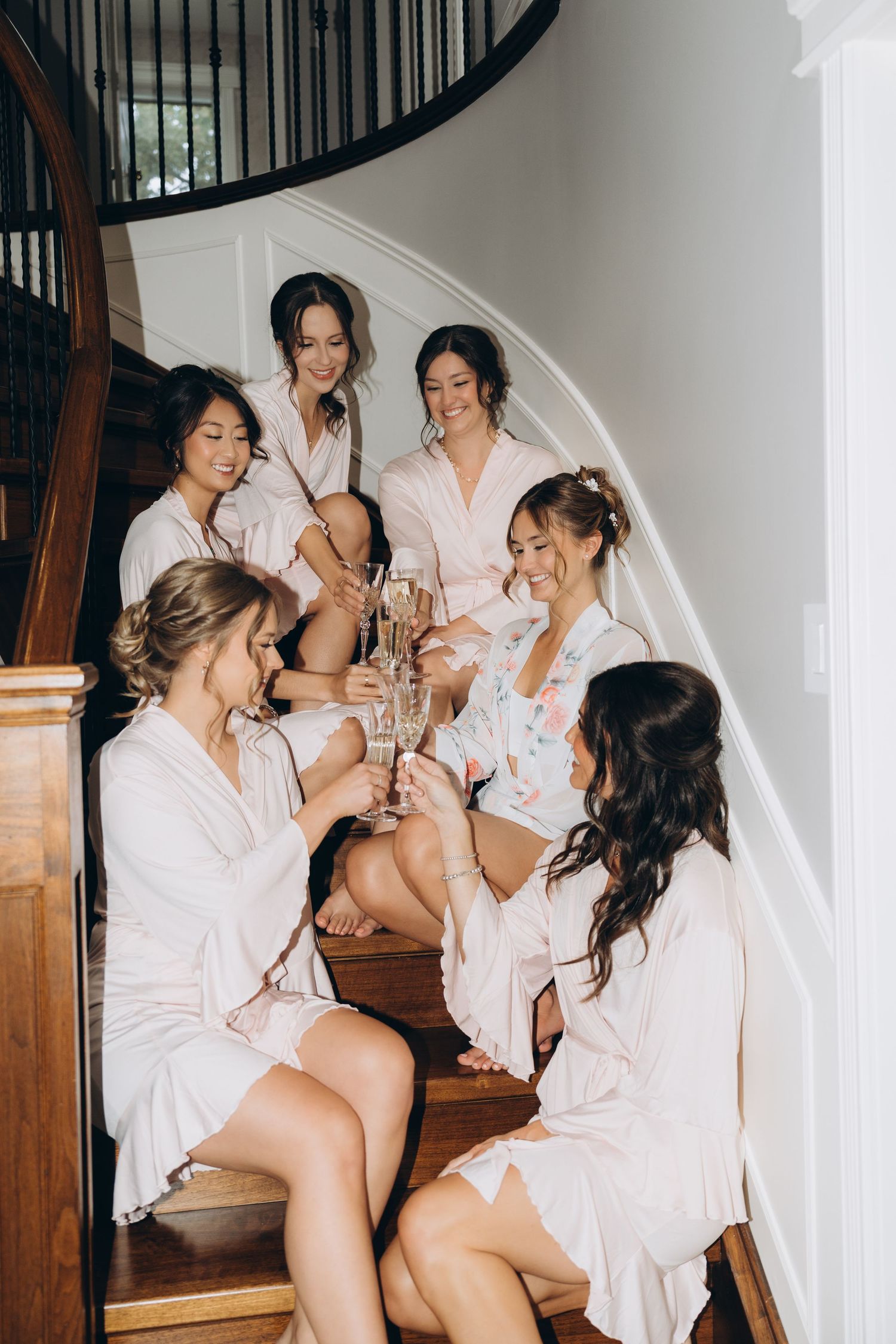 A group in matching white robes sits on wooden stairs while sharing drinks and laughter during a celebration.