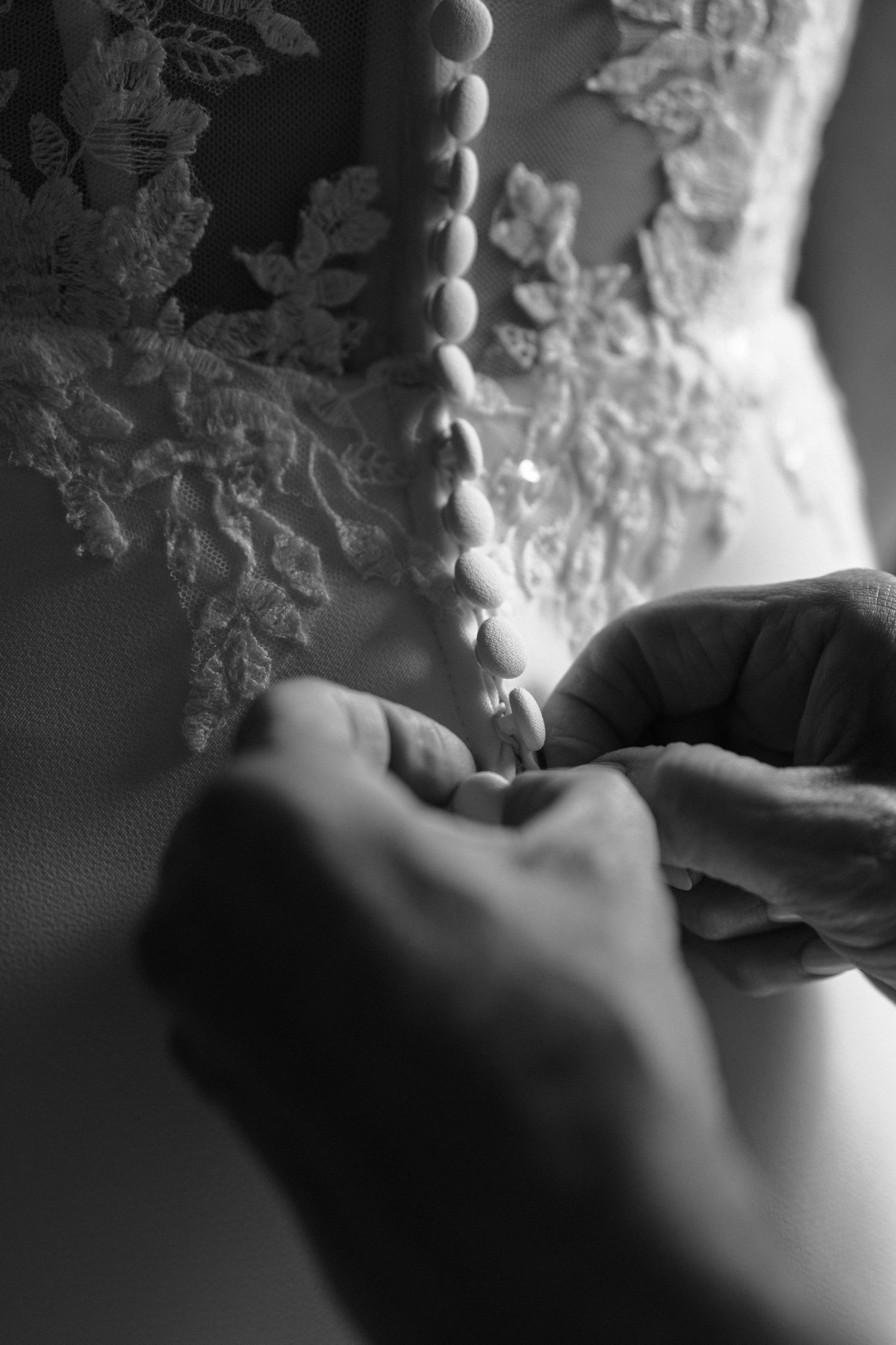 A black and white close-up photograph showing someone writing in a book with delicate lace details visible in the background.