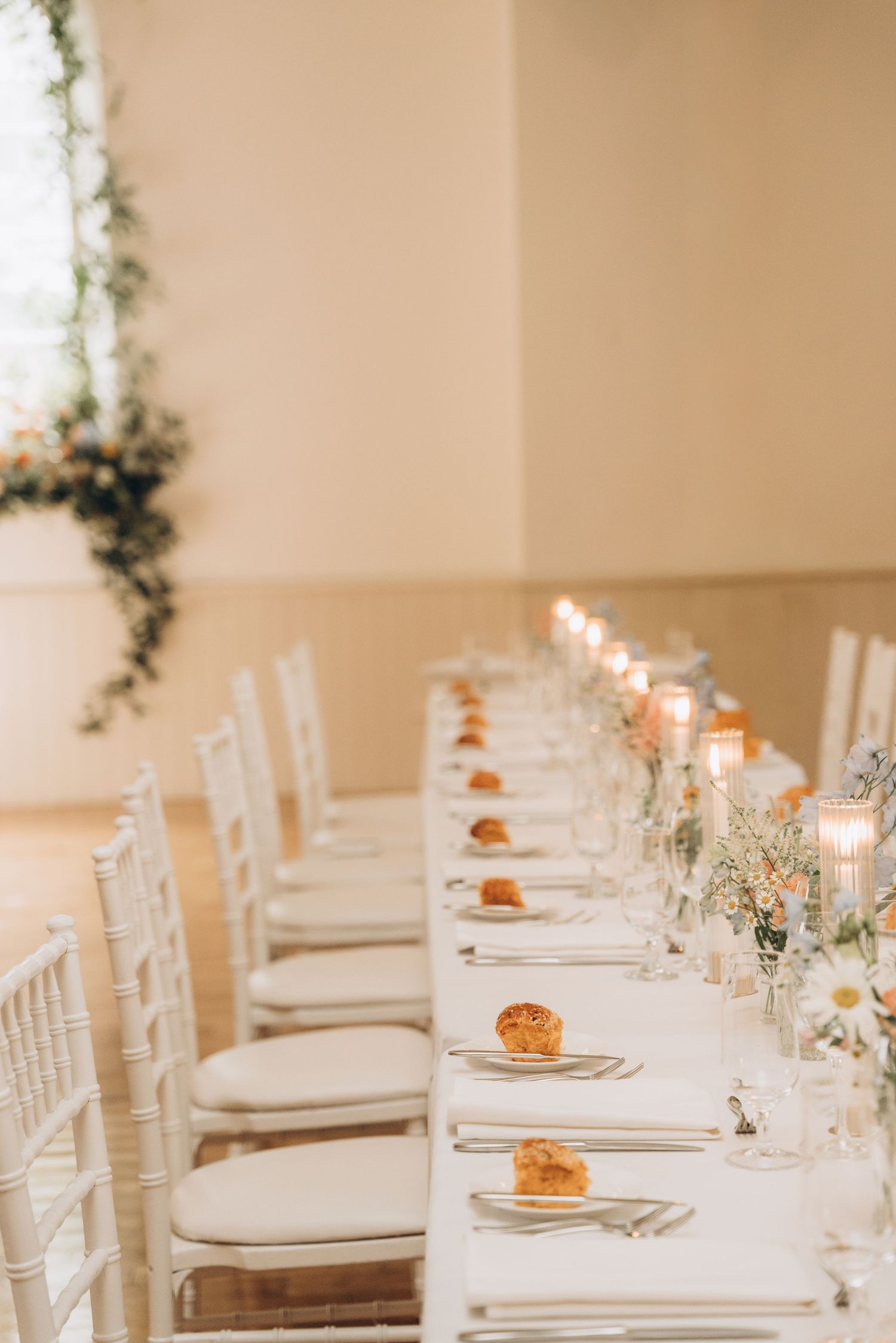 Elegant wedding reception table setting with white linens, candles and floral centerpieces in a bright indoor venue.