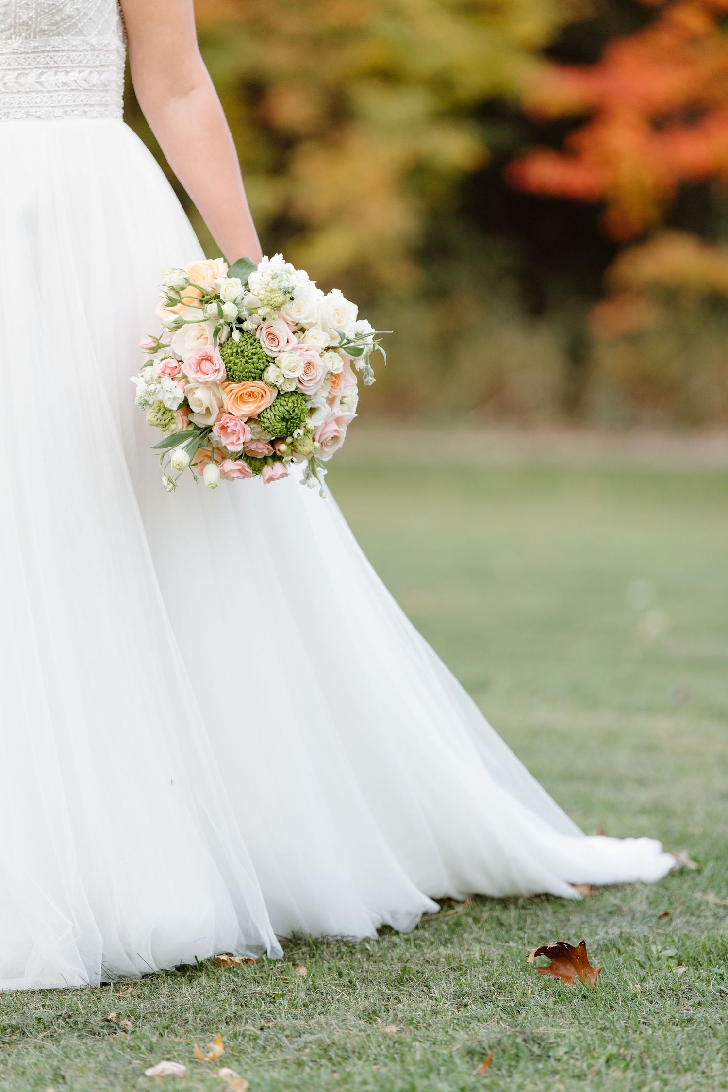 Close-up of bridal bouquet with pink and white flowers against white wedding dress hem.