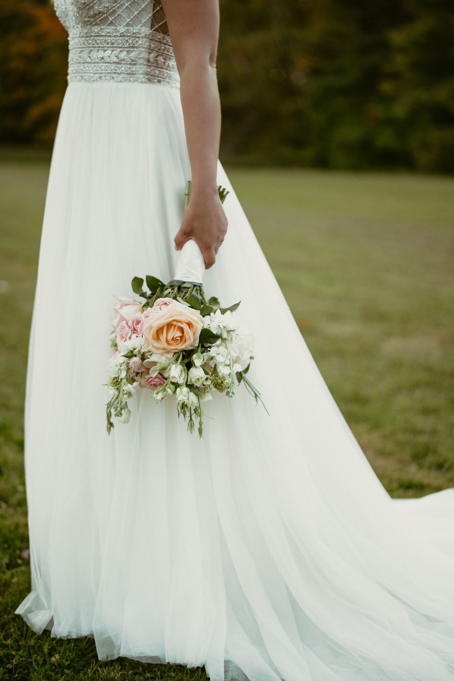 Close-up detail of a wedding dress with a delicate bouquet featuring peach roses and greenery.