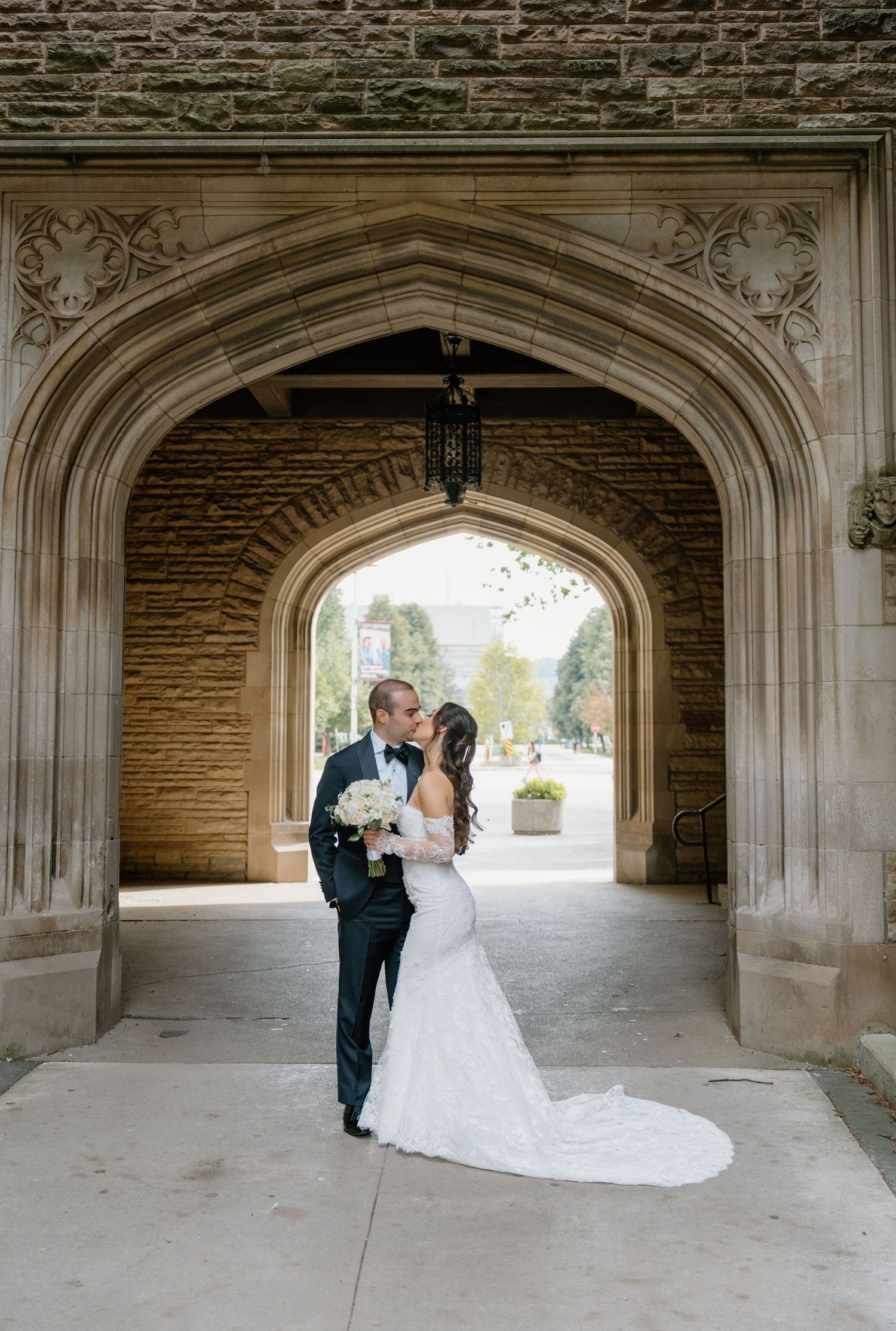 A romantic wedding photoshoot under a stone archway with a long white dress trailing on the ground.