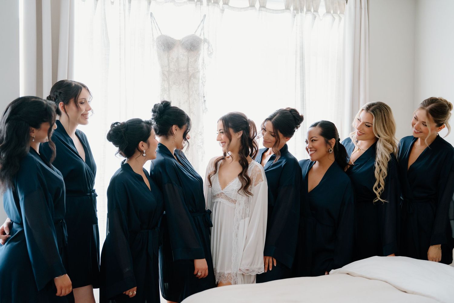A series of wedding guests stand in a line against a white wall during a formal celebration.