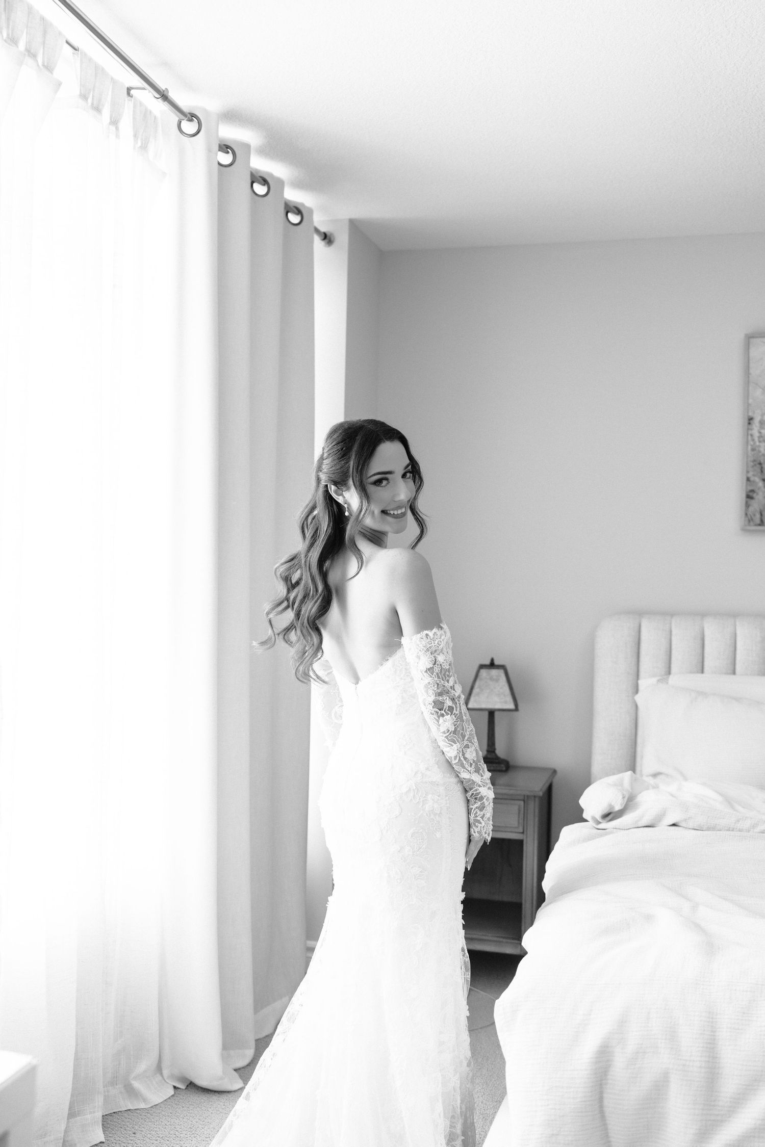 Black and white wedding photos showing a bride in a lace gown in a bright bedroom setting.