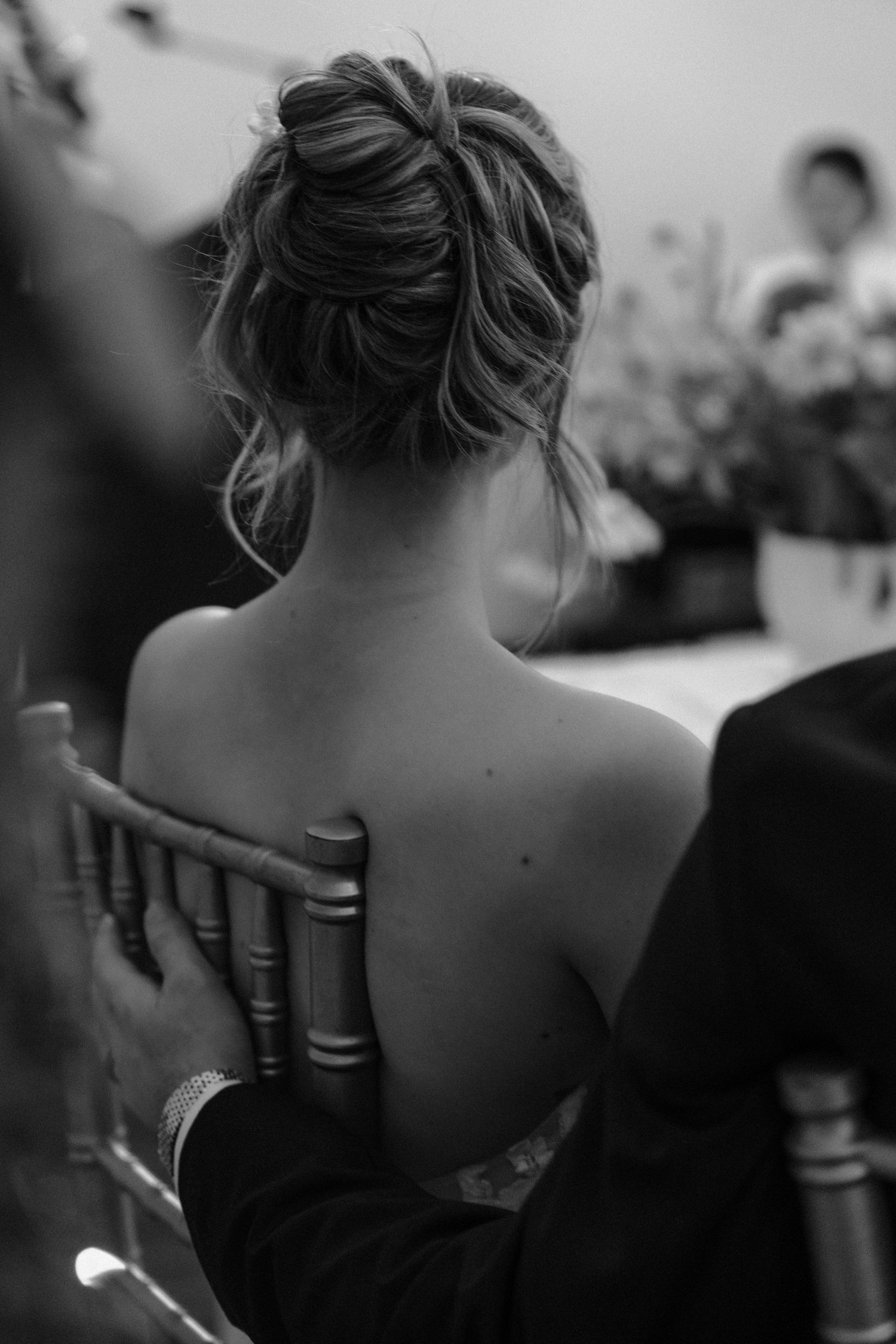 Black and white close-up photograph showing the back of someone's neck and shoulders with a strapless dress.