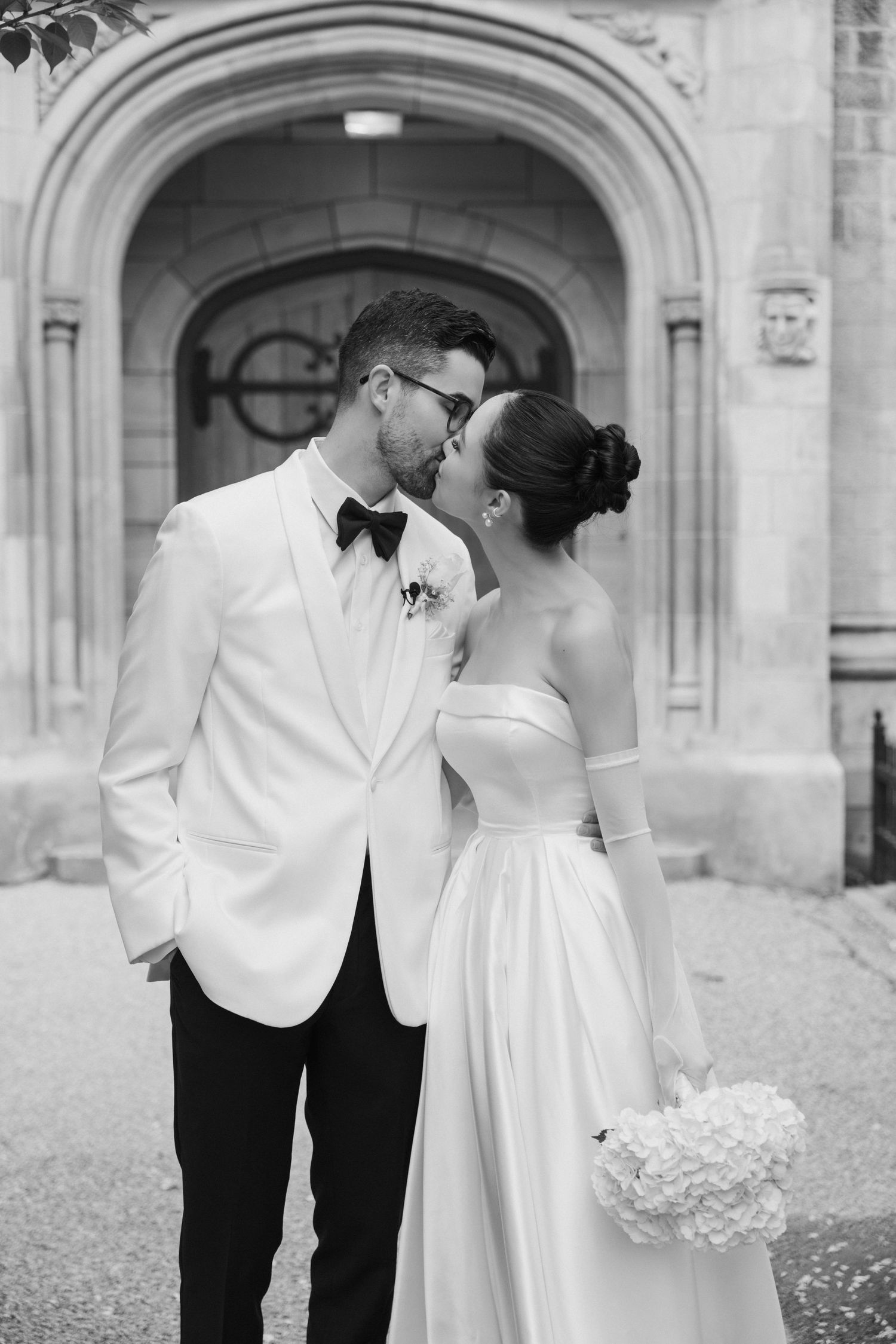 Elegant black and white wedding photo of couple sharing intimate moment under arched doorway in classic attire.