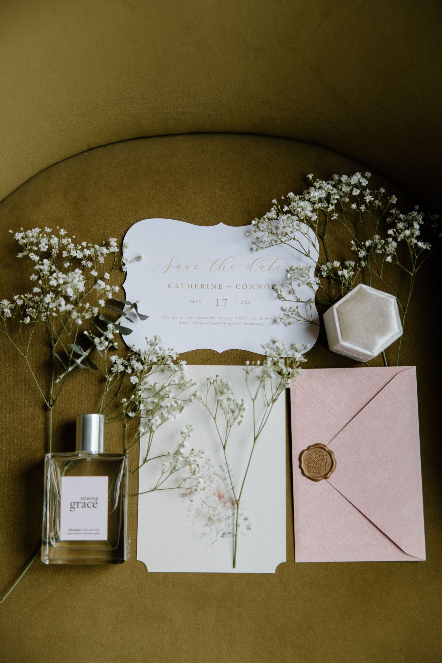 Wedding invitation suite in blush pink and white with baby's breath flowers and wax seal displayed in a flat lay composition.