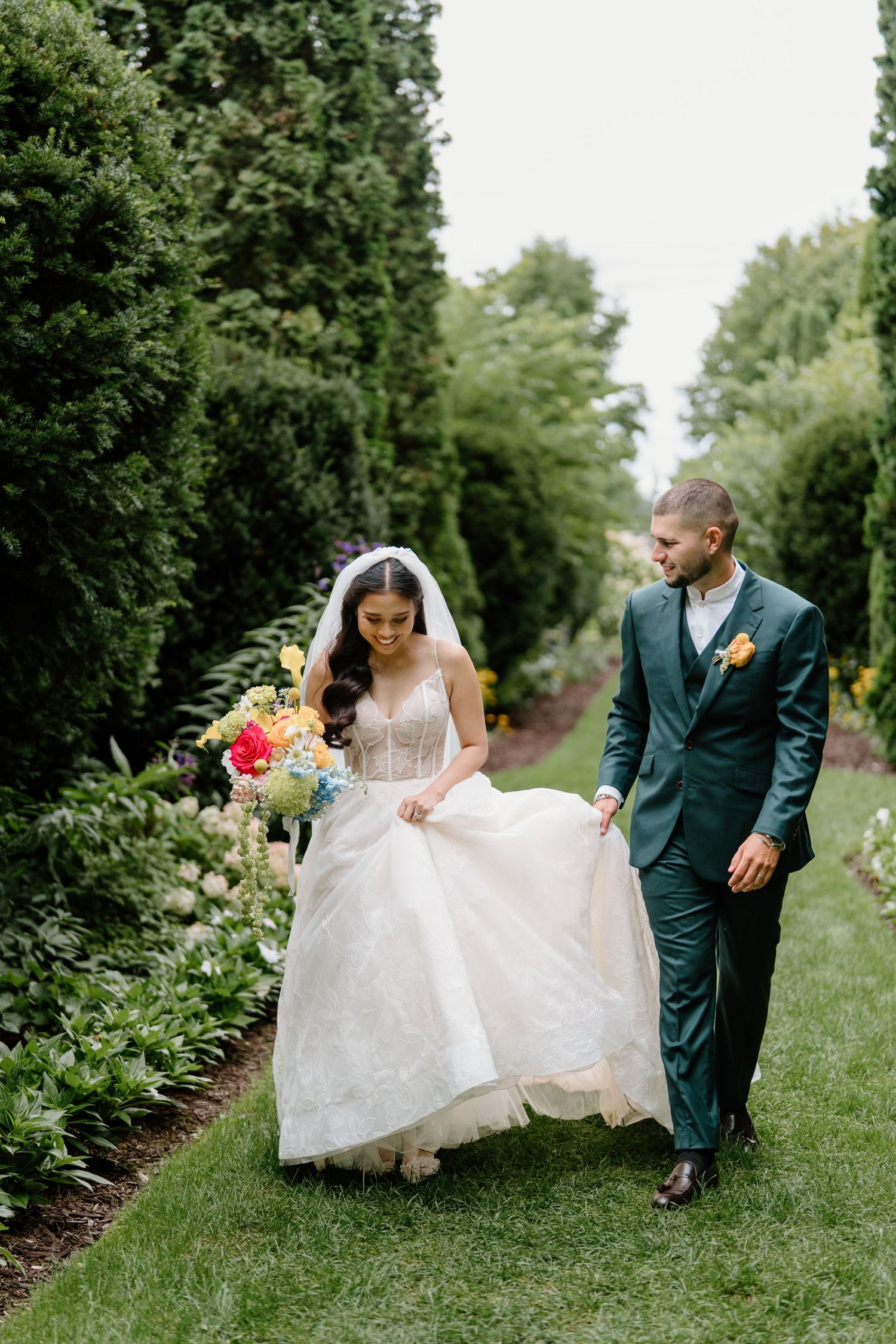 A romantic wedding couple walks together through a lush green garden path in a sequence of candid moments.