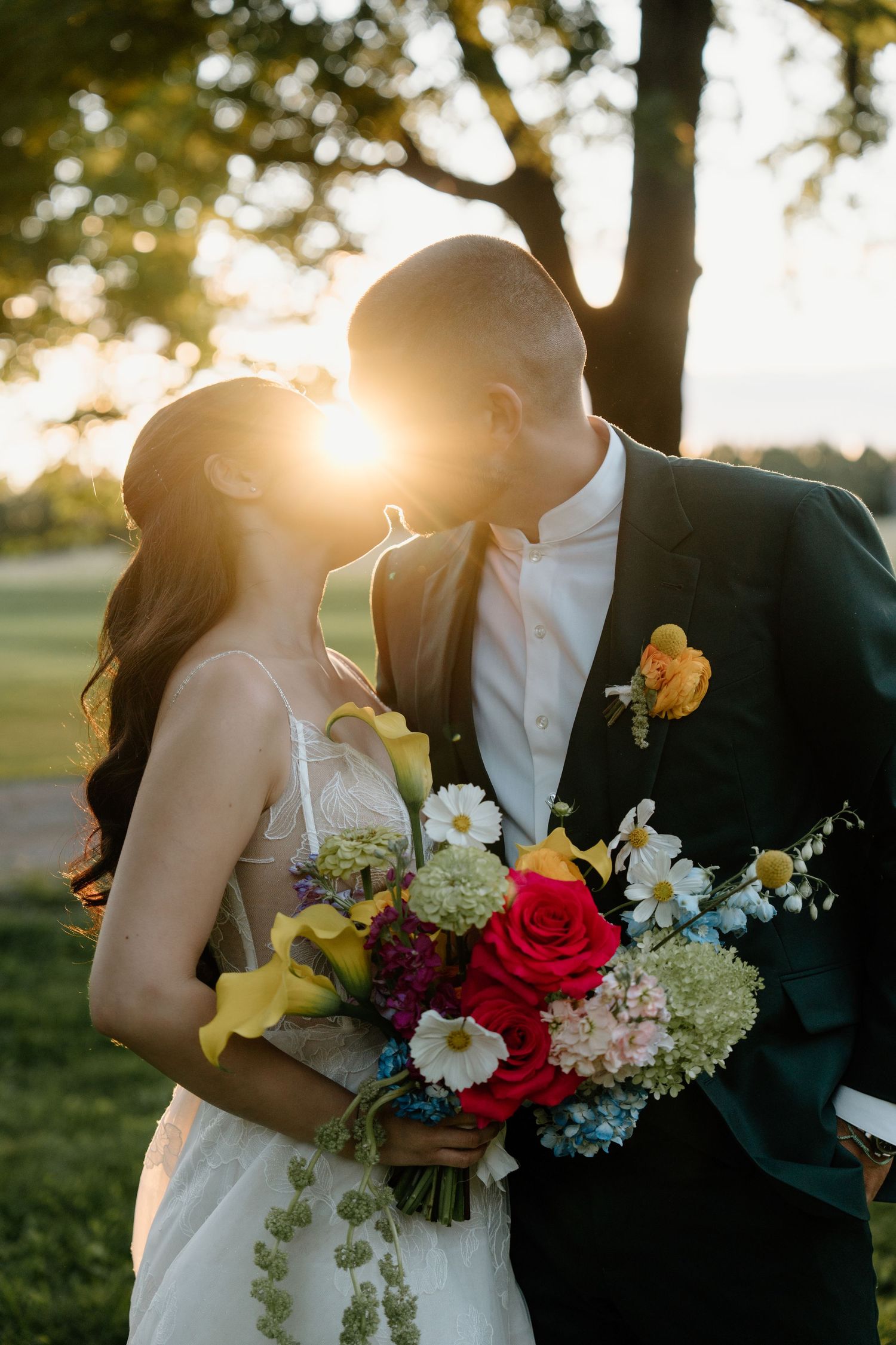 Wedding couple shares intimate moment outdoors with vibrant floral bouquet at sunset.