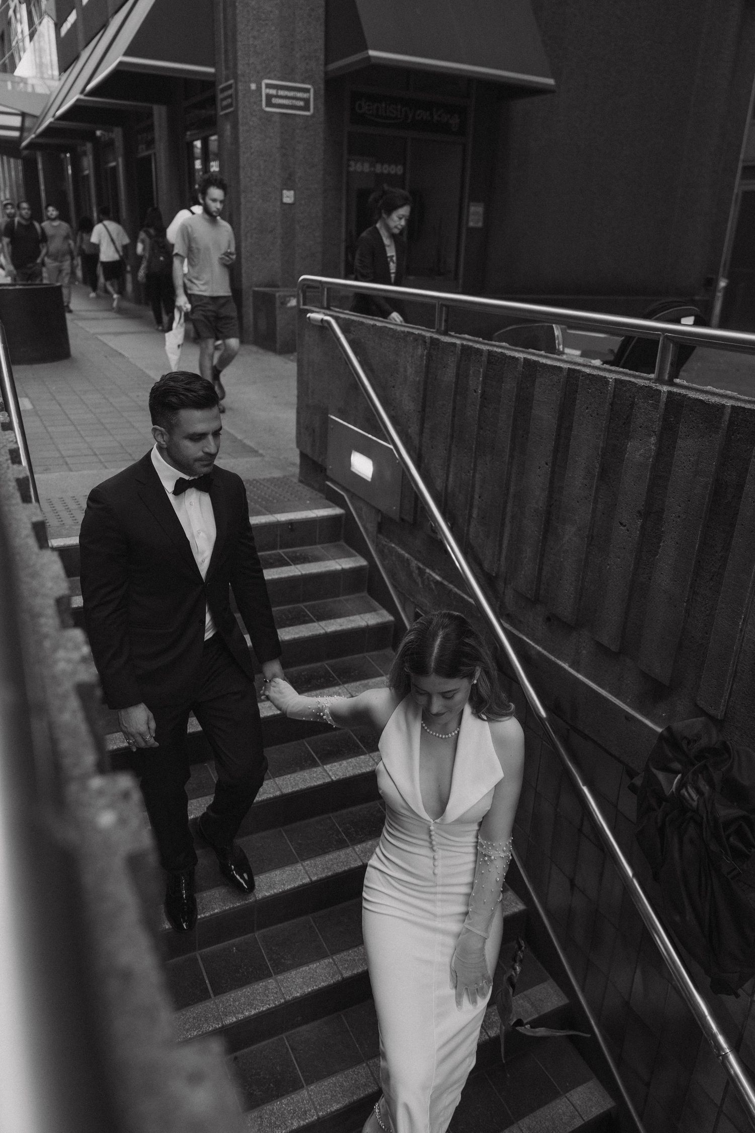 A couple in formal attire descend outdoor stone steps in an urban setting.
