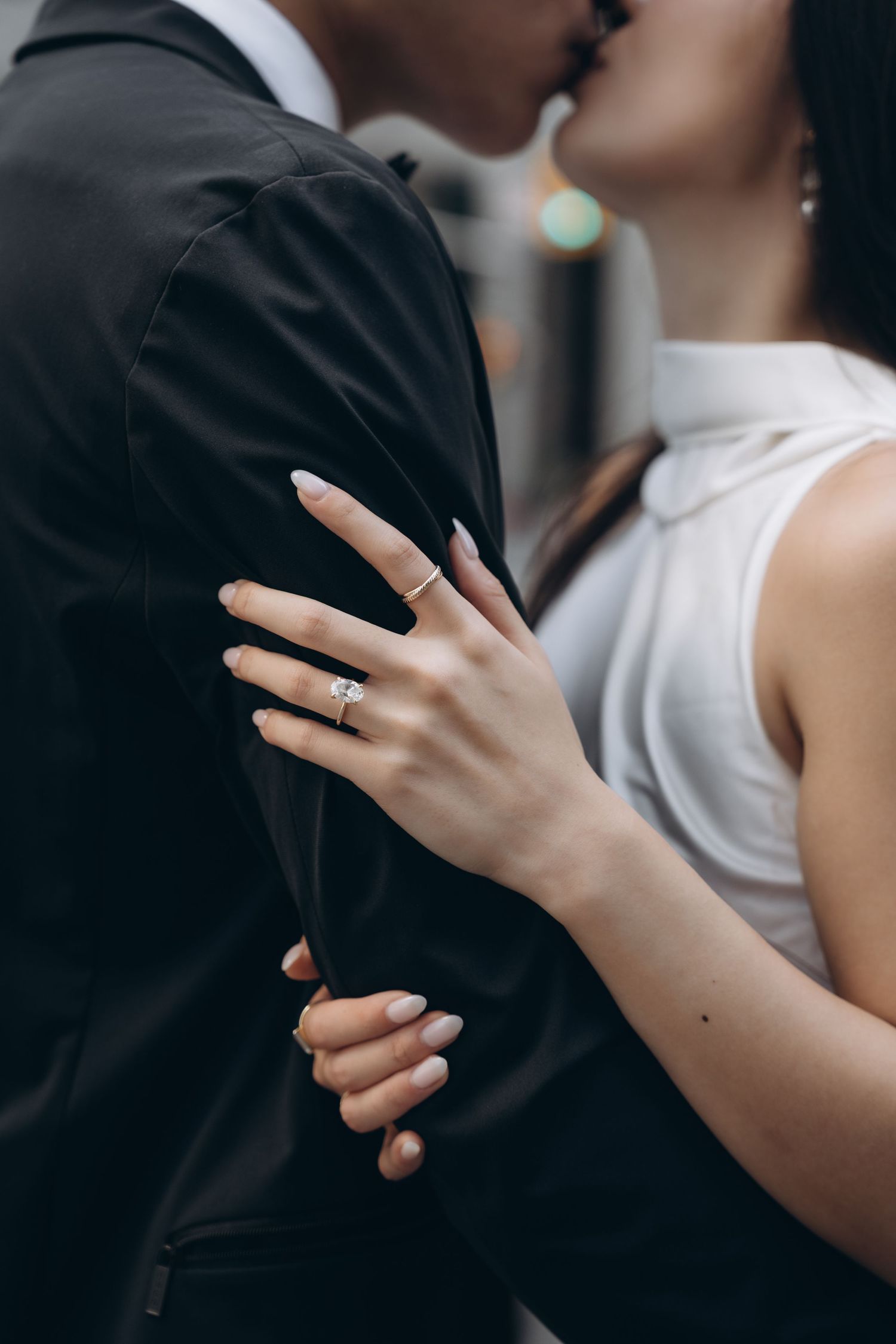 Close-up photo of an engagement ring on the hand of someone in white embracing a person wearing black.