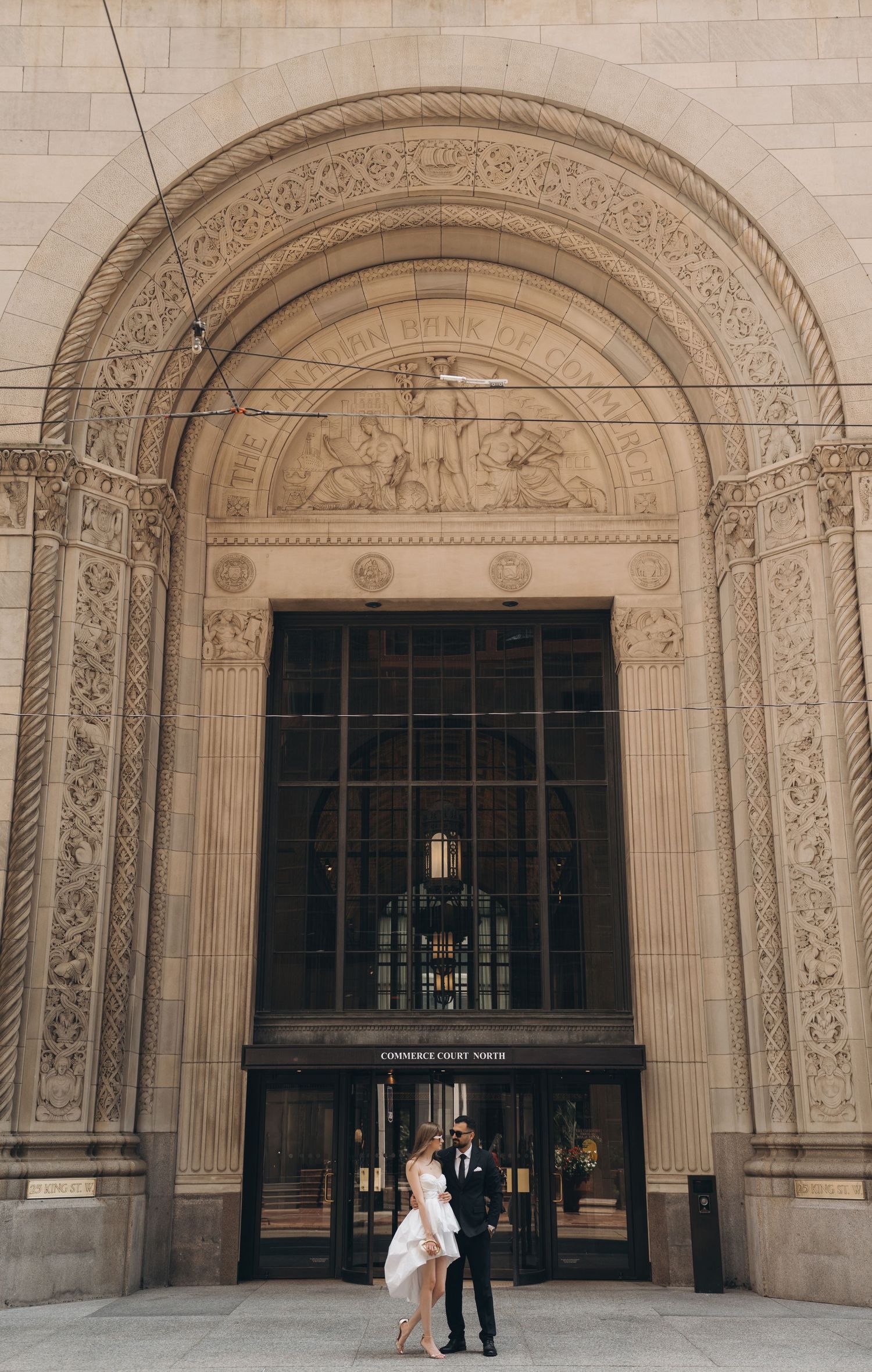 People standing beneath grand stone archways in a formal architectural setting with decorative details.