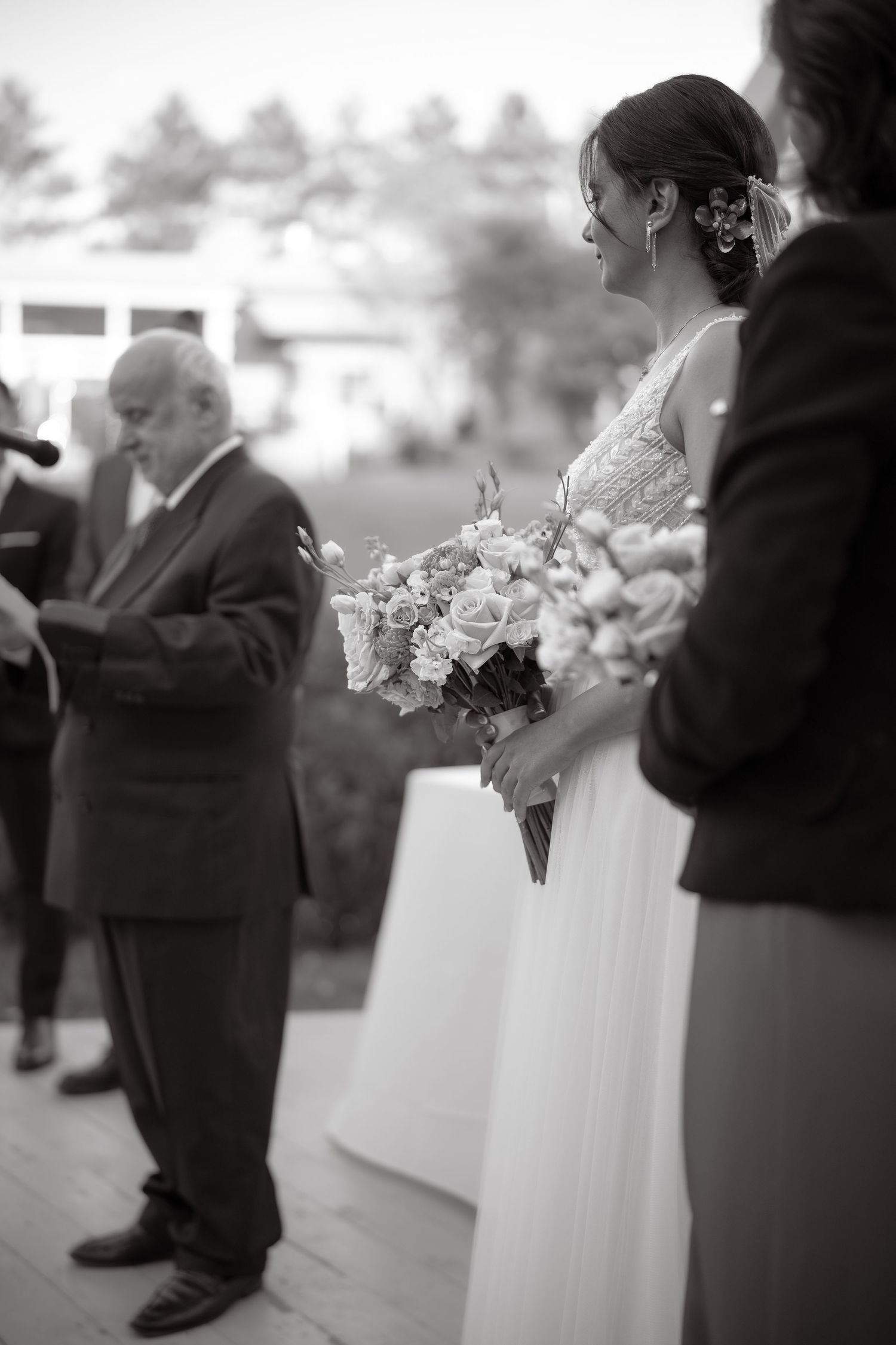 Black and white photo of a wedding ceremony with floral bouquet and outdoor setting.