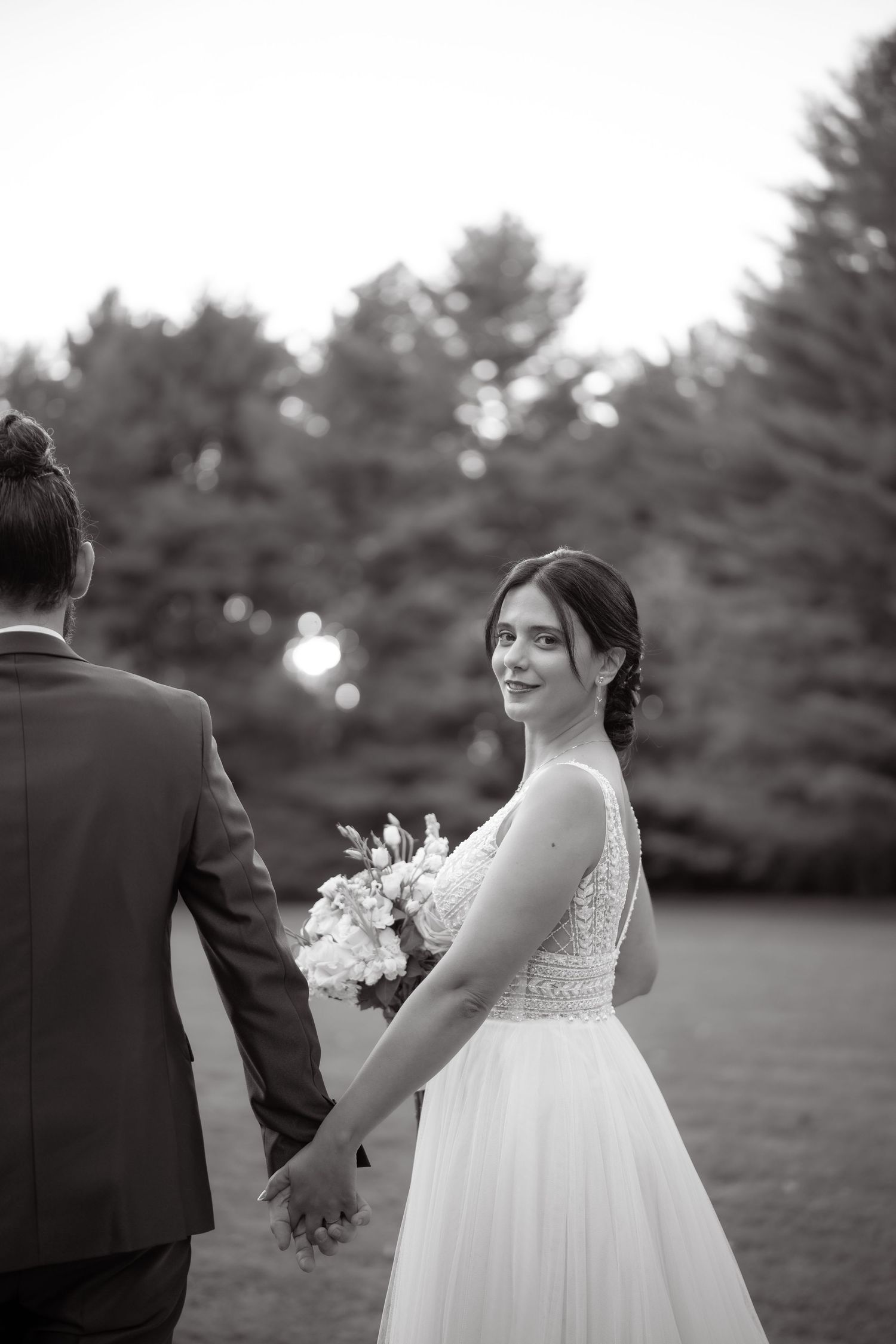 Intimate black and white wedding portrait on lawn with evergreen backdrop.