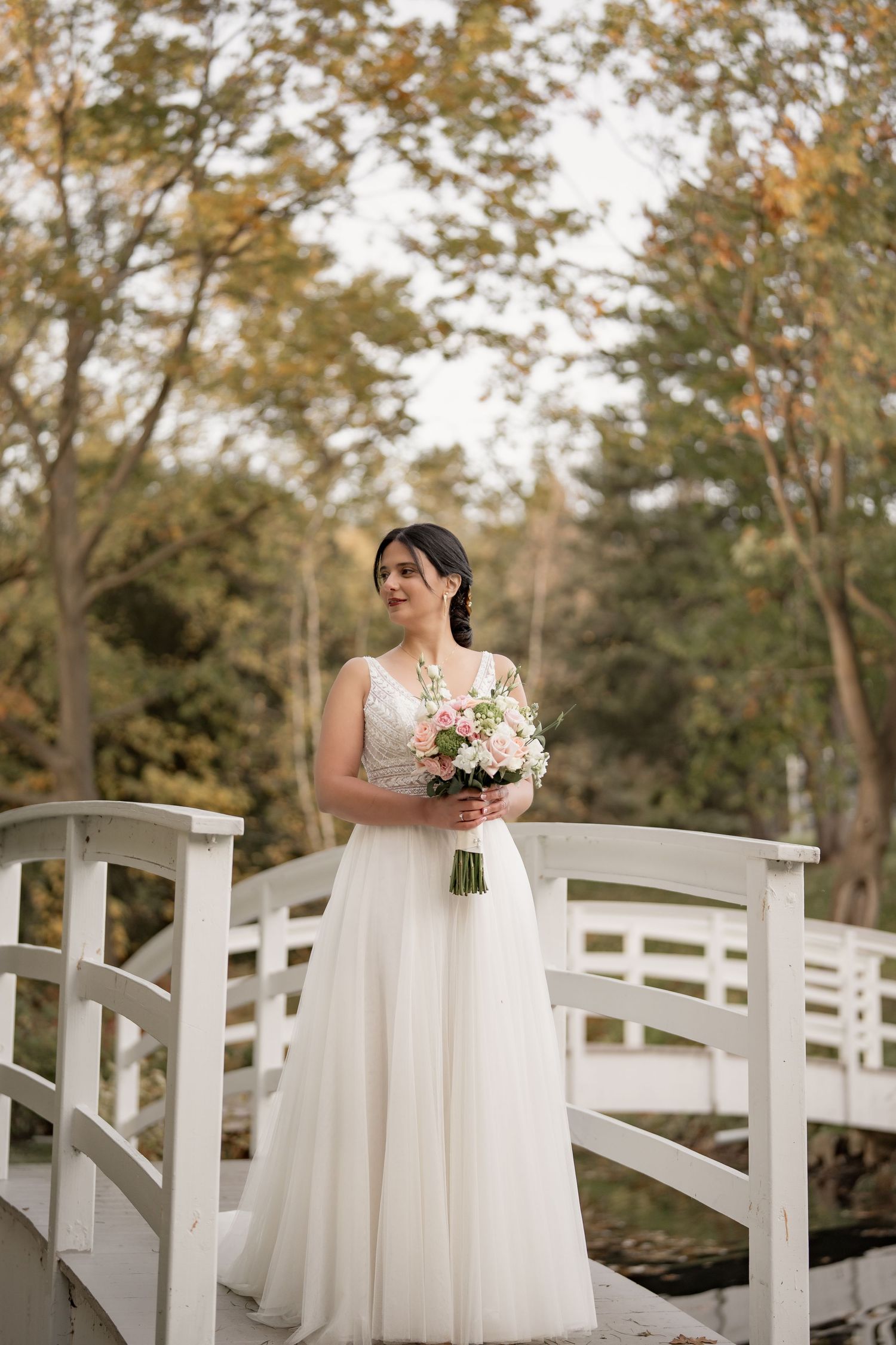 Bridal portrait on a white bridge showcasing a flowing dress and soft pink bouquet.
