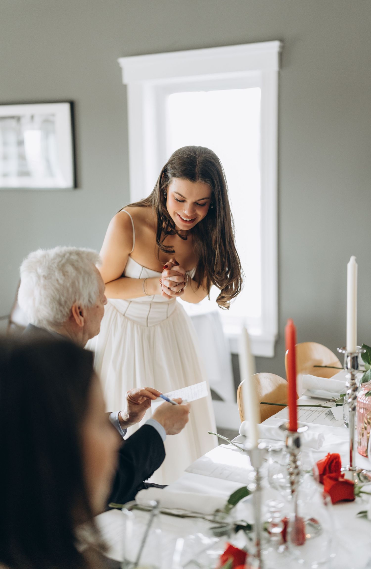 Woman in white dress interacting with guests during a formal dinner party with red candles and elegant table settings.