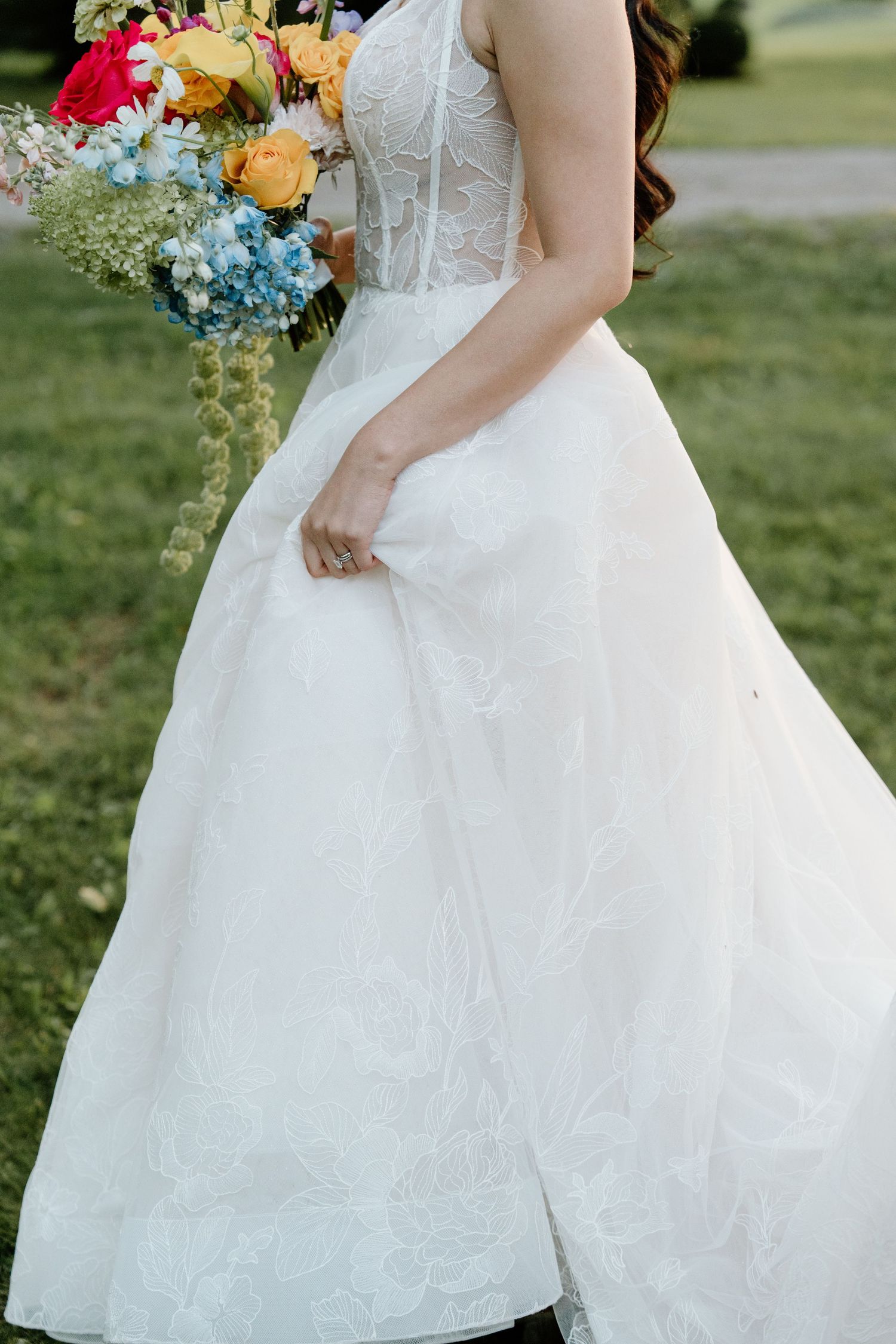 Close-up details of a flowing white wedding dress with colorful floral bouquet accents.