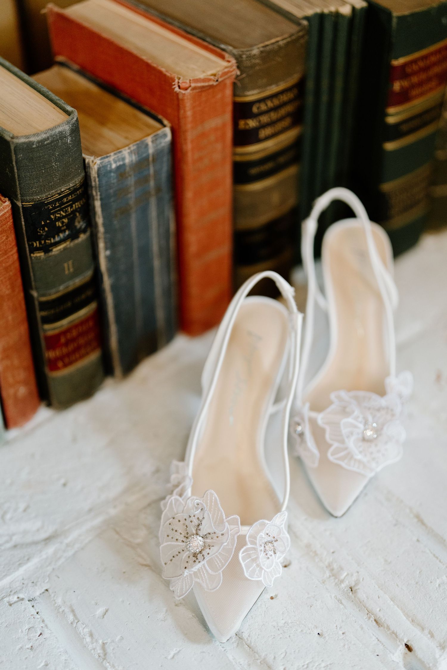 Elegant white lace bridal shoes displayed against vintage books on a rustic white surface.