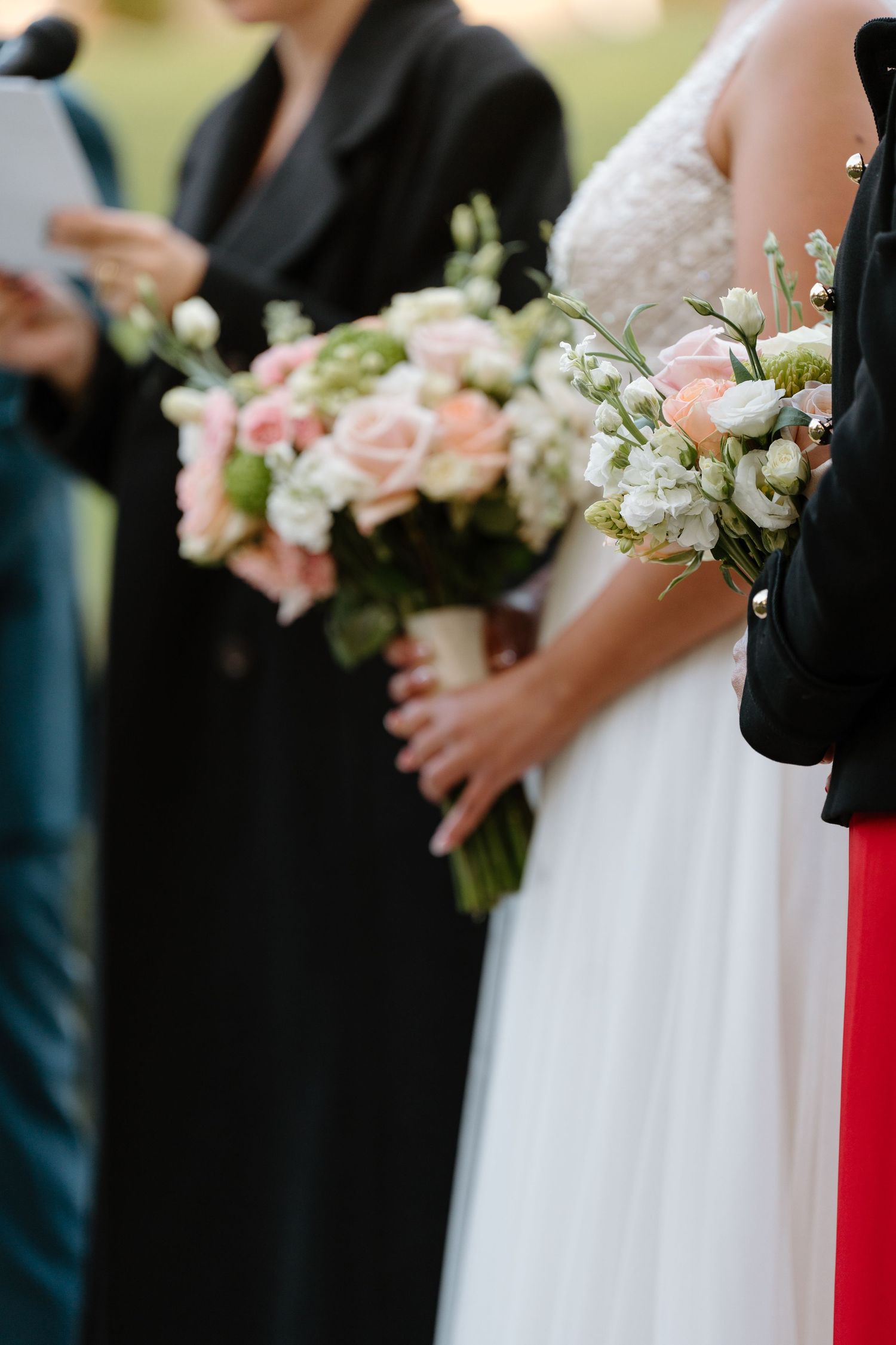 Wedding bouquet with pink roses and white flowers held against formal attire.