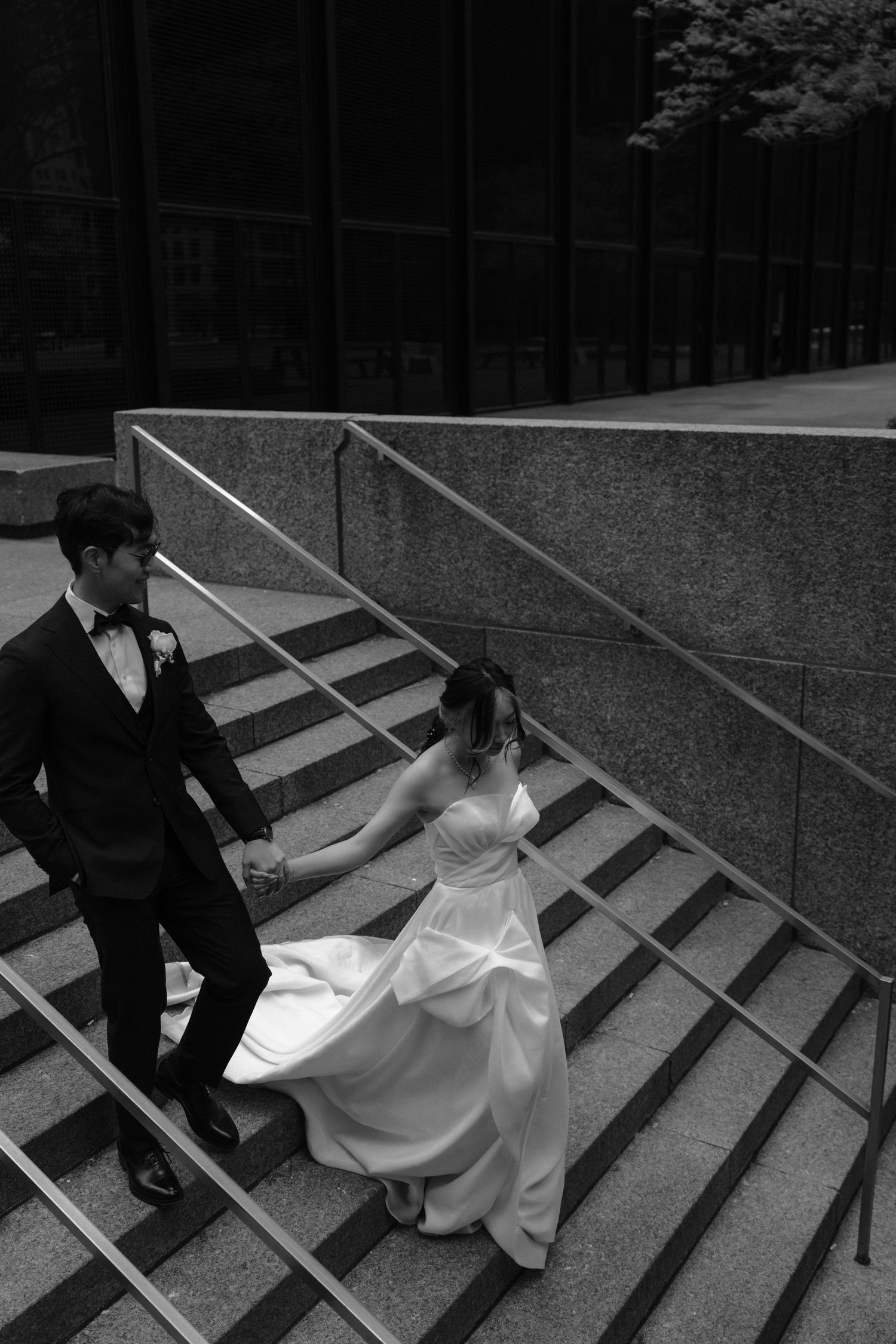 A bride and groom walk down a set of concrete steps in a elegant black and white wedding photo.
