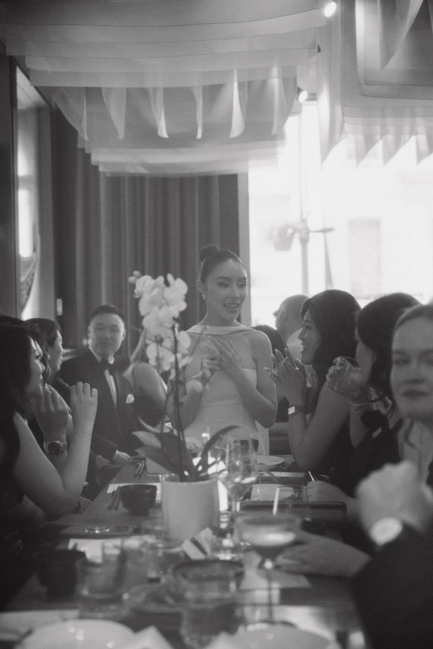 Black and white photo showing guests seated at tables during an indoor celebration with white banners hanging from the ceiling.