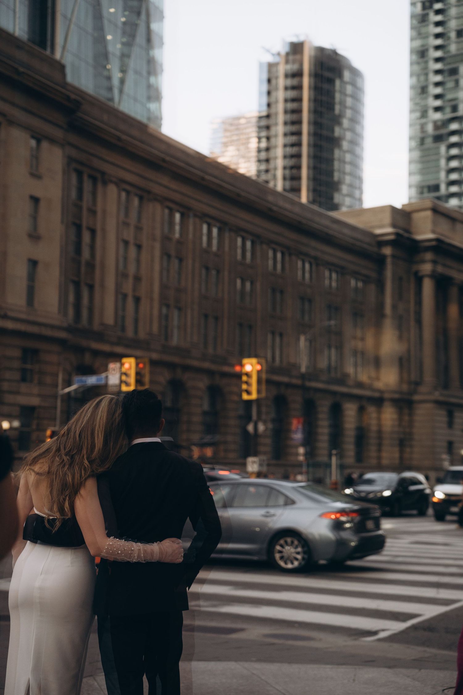 Two figures in black and white embrace on a city street with tall buildings and urban architecture in the background.