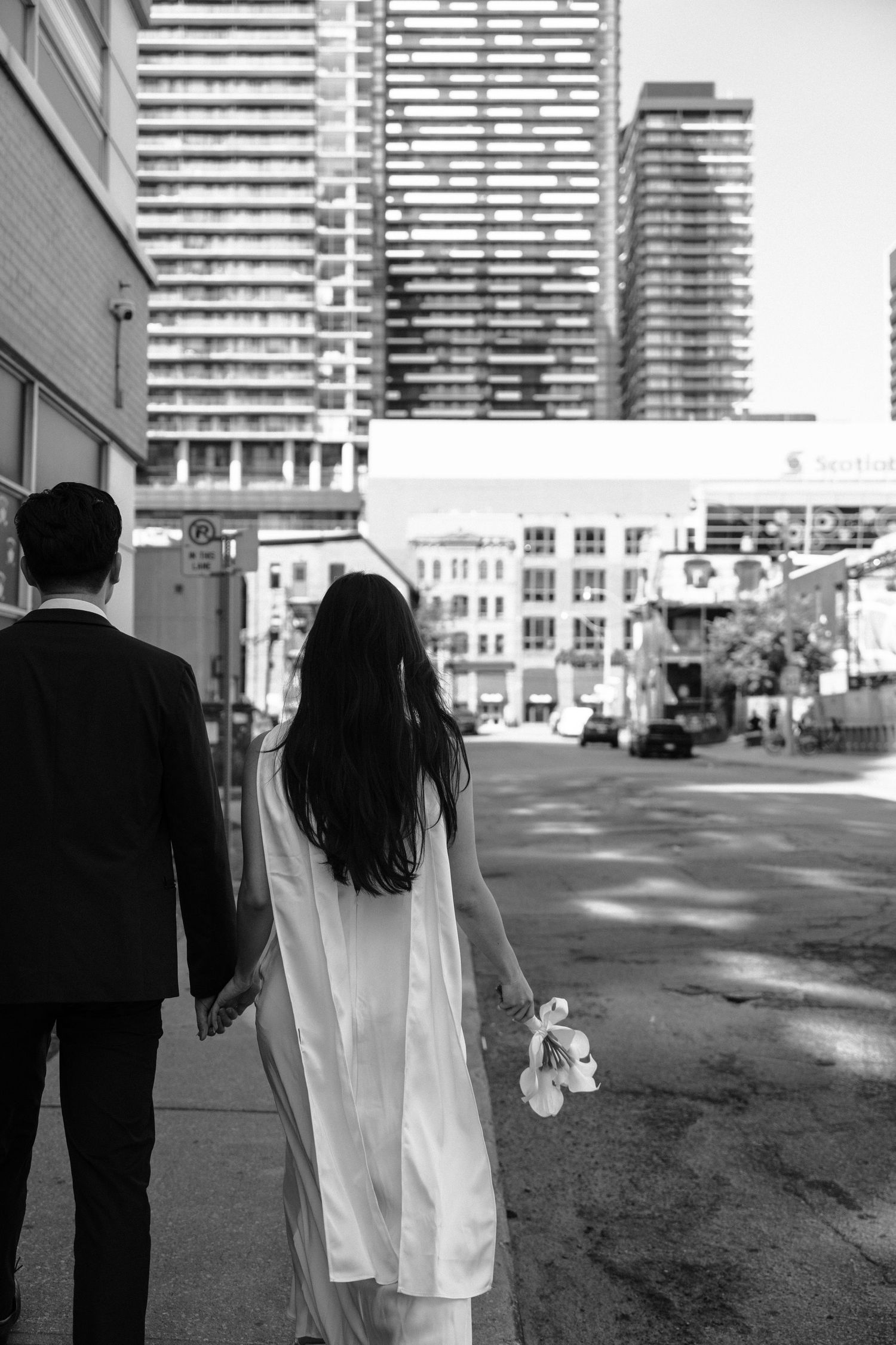 A cinematic sequence of a bride and groom walking away down a city street with high-rise buildings in the background.