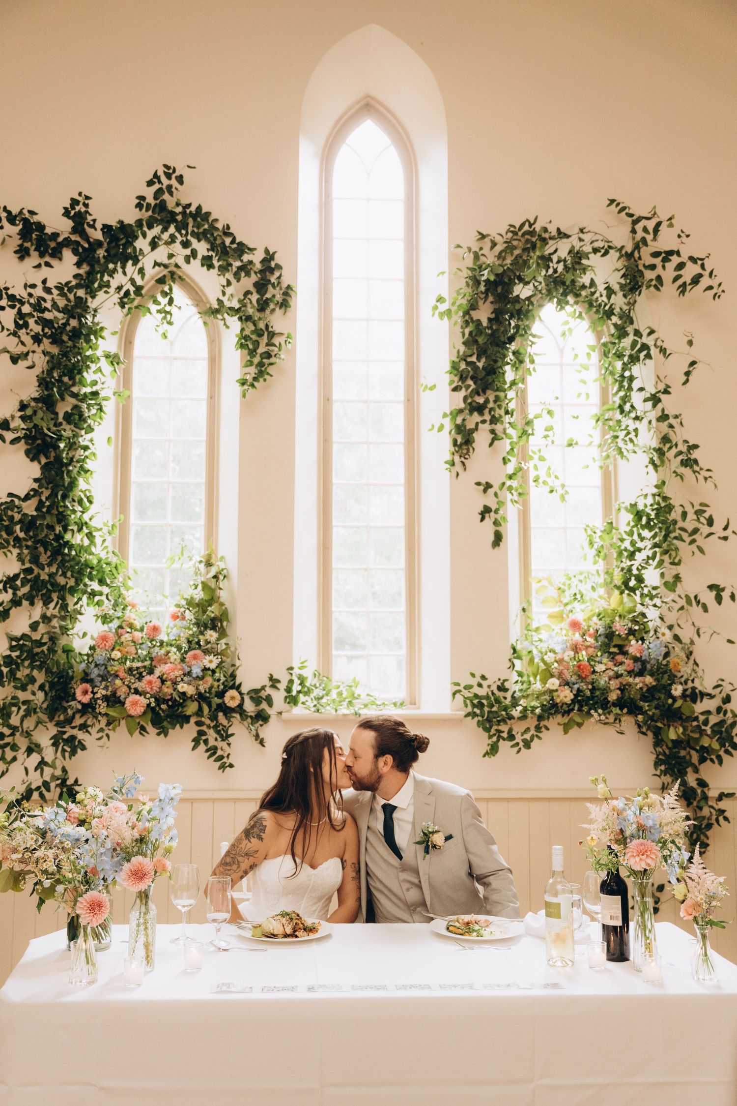 A romantic scene in a chapel with arched windows decorated with lush greenery and floral arrangements.