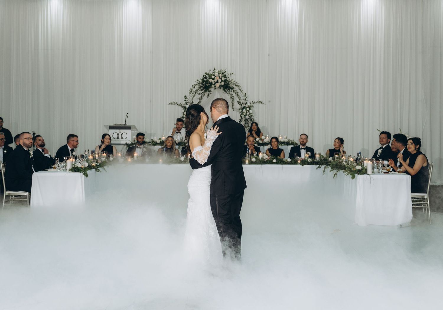 A couple shares their first dance at a wedding reception with fog effects and dramatic lighting on the dance floor.