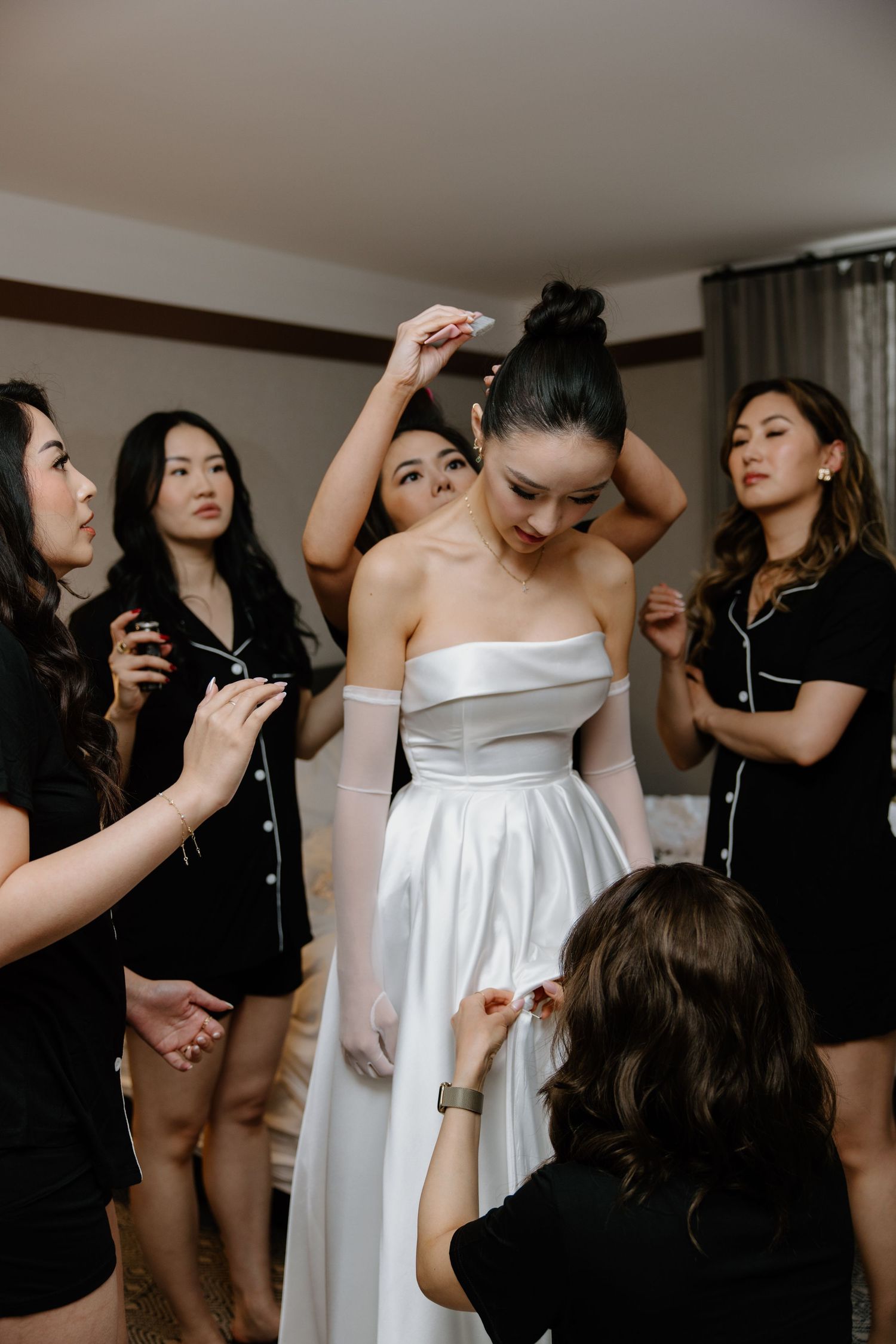 A group of women help with bridal preparations in a modern getting ready room.
