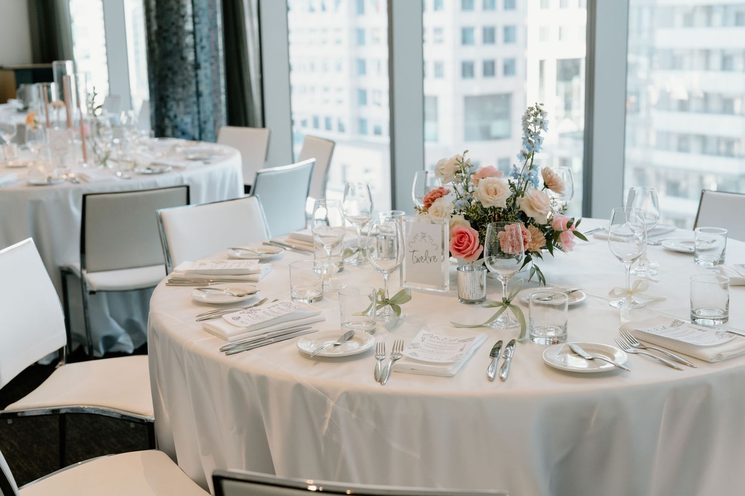 Round dining tables adorned with white tablecloths, place settings, and floral centerpieces in an elegant restaurant space.