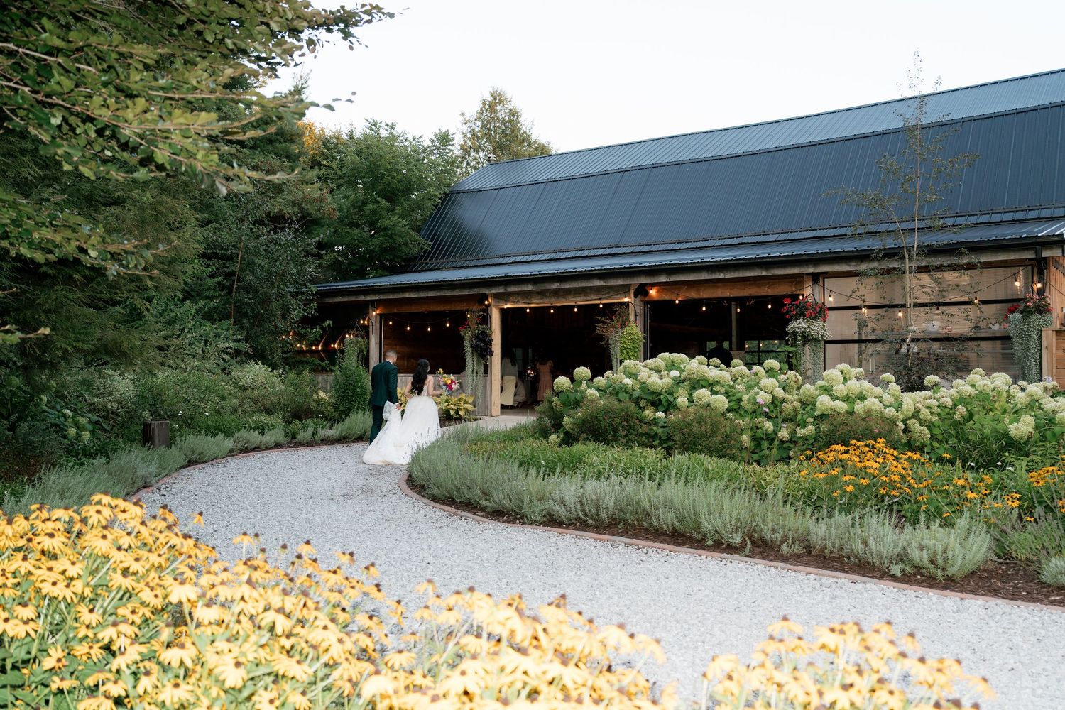 Curved pathway leads through a landscaped garden with yellow flowers and modern buildings in the background.