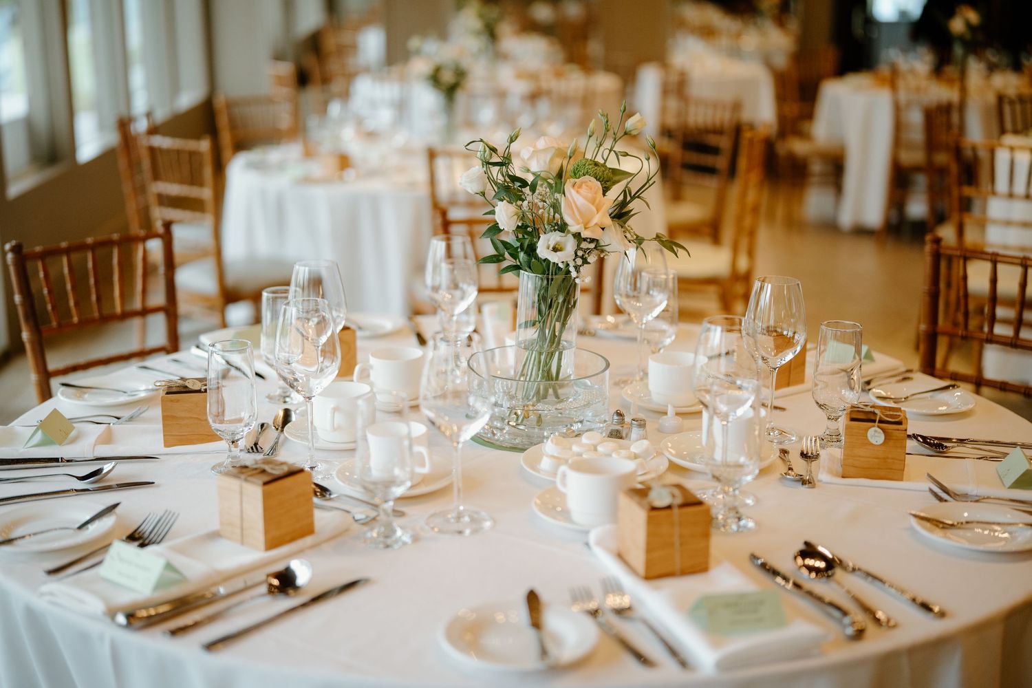 Elegant wedding reception table setting with white linens, gold favors, and delicate floral centerpieces.
