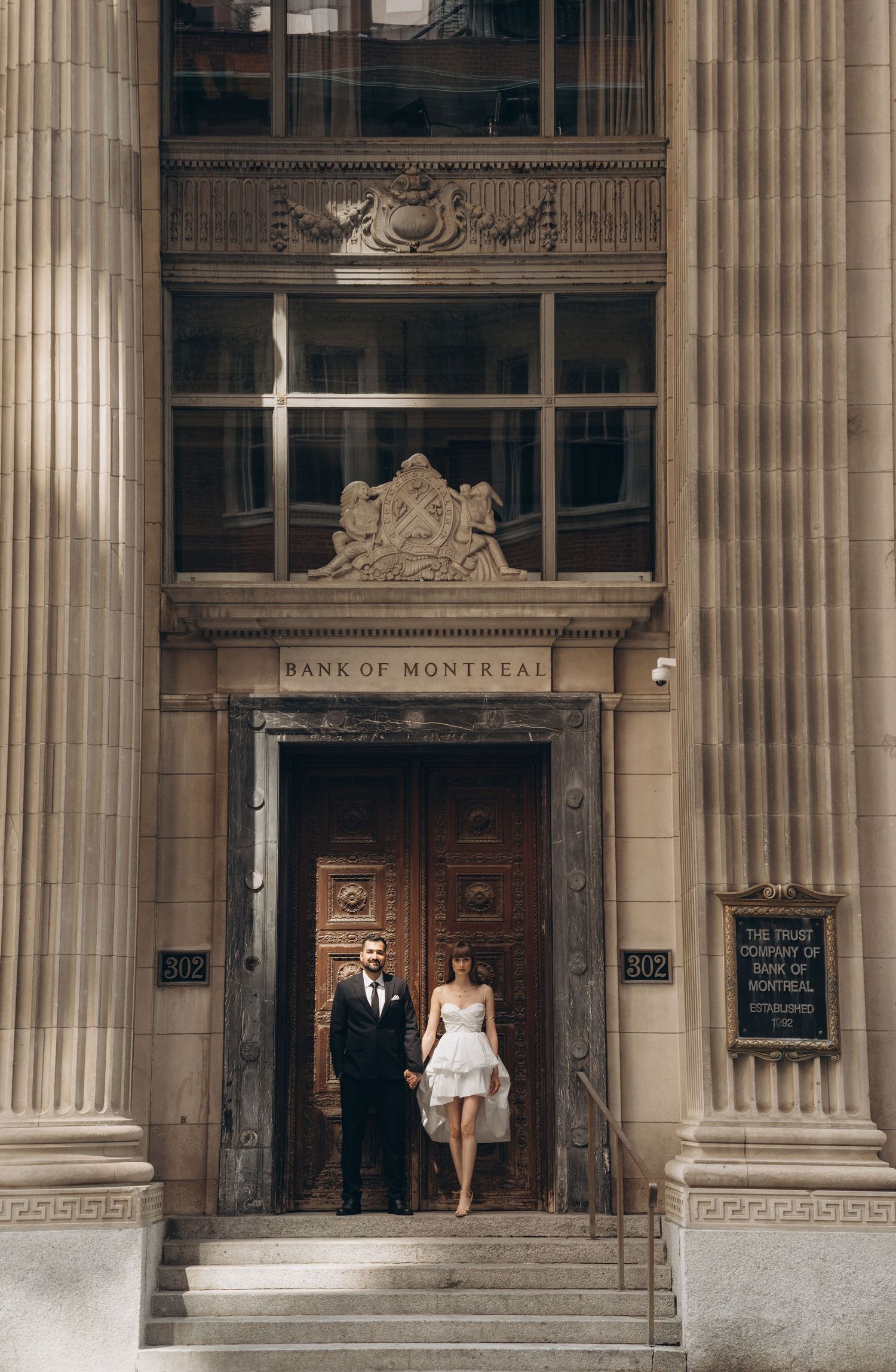 A couple stands at the entrance of a neoclassical building with towering stone columns.