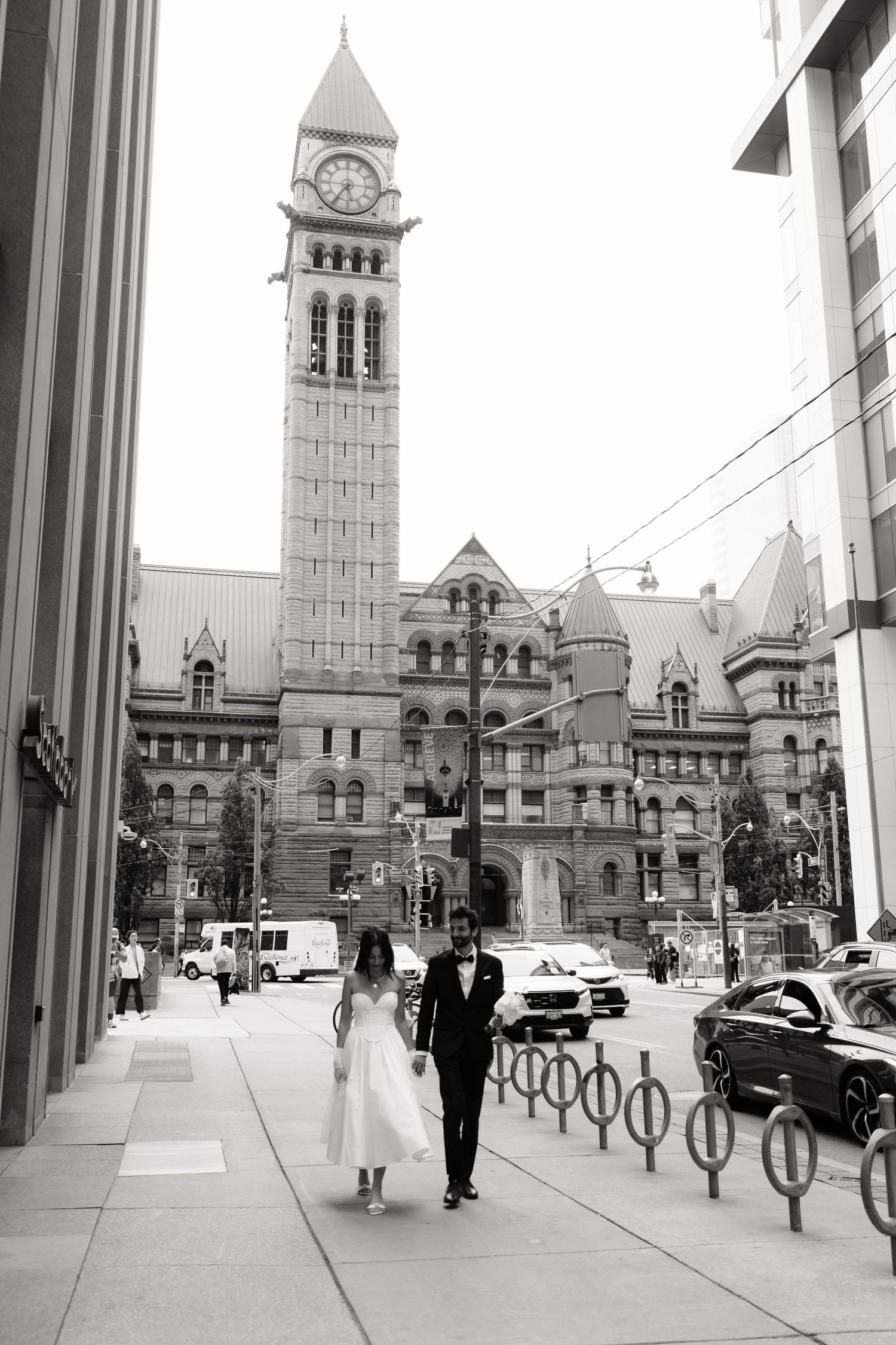 Black and white panoramic sequence of a historic city hall building with clock tower and pedestrians walking by.