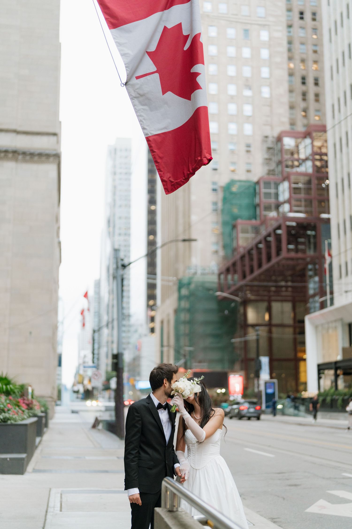 A couple shares a romantic moment under a waving Canadian flag in downtown Toronto's urban setting. in Toronto by AZ Photo Studio.