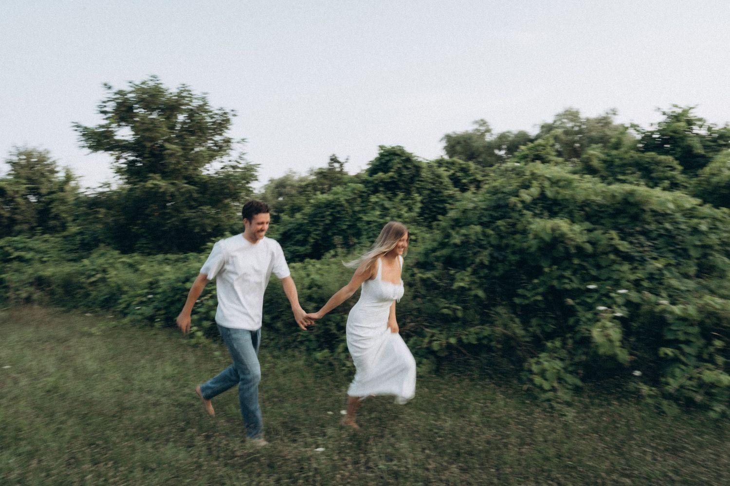A couple holds hands while walking through a lush green meadow on a summer day.