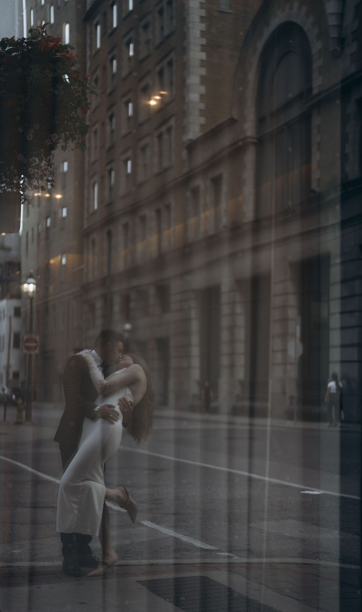 A couple shares a romantic embrace on a moody city street with historic architecture and soft lighting in the background.