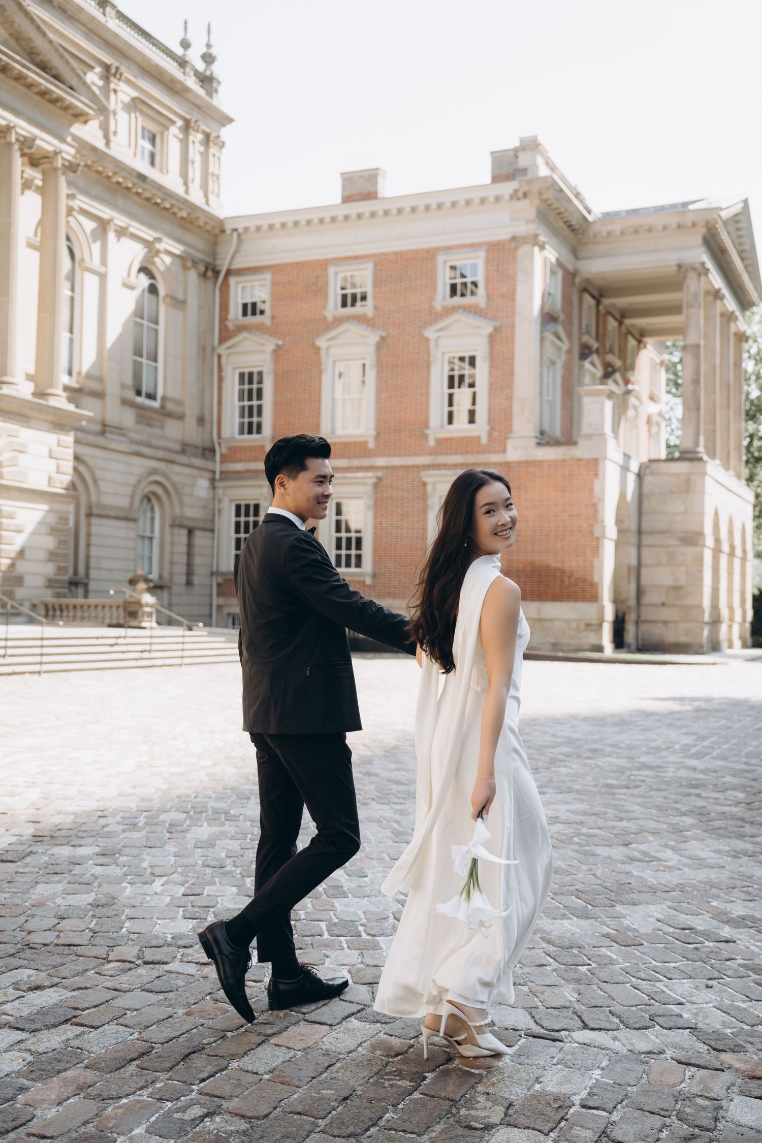 Romantic photo series showing a couple walking and posing across a historic European courtyard with grand architecture.