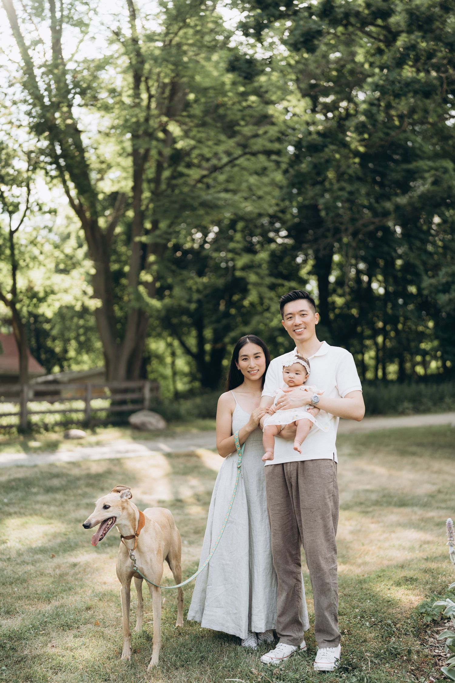 A family poses with their whippet dog in a sunny outdoor setting with trees in the background.