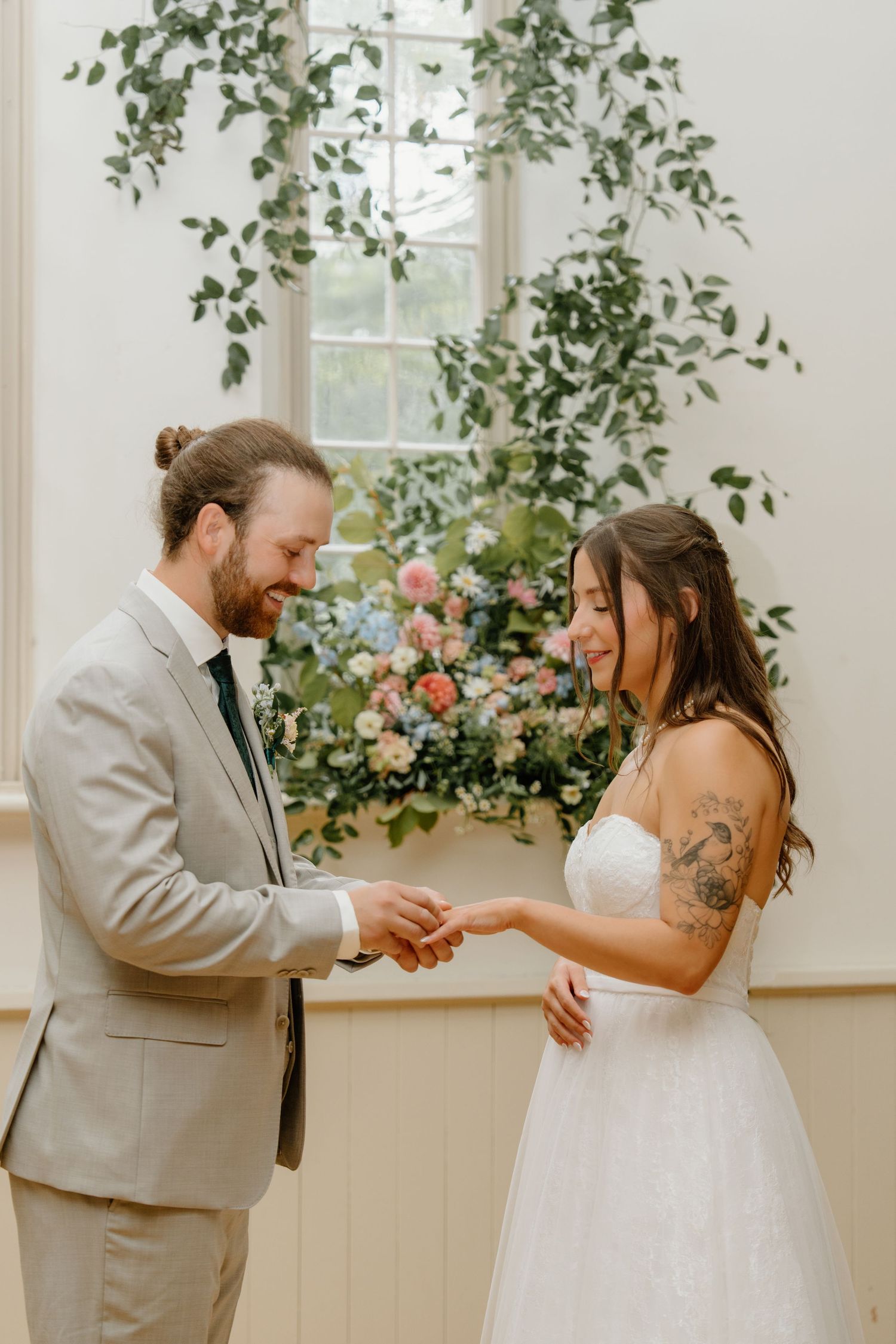 A couple shares a joyful dance moment in a light-filled room decorated with hanging greenery and florals.