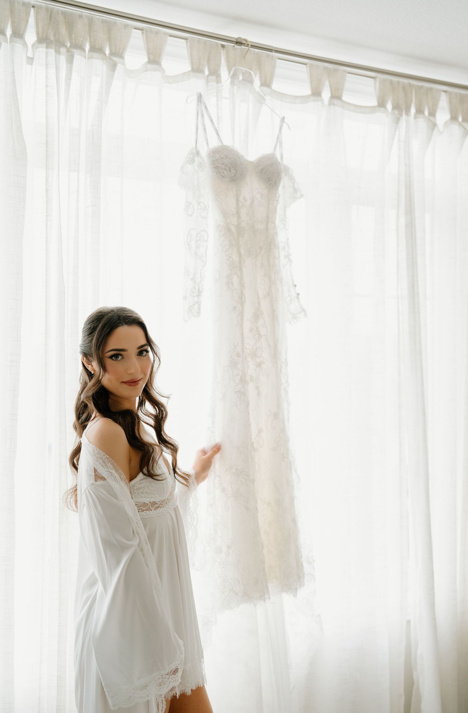 A dreamy boudoir photoshoot with soft white curtains and natural window light creating an ethereal atmosphere.