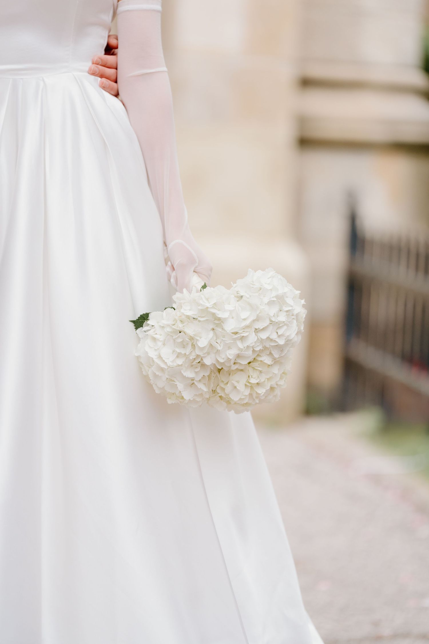 A white wedding dress with elegant long sleeves is paired with a beautiful bouquet of white hydrangeas.