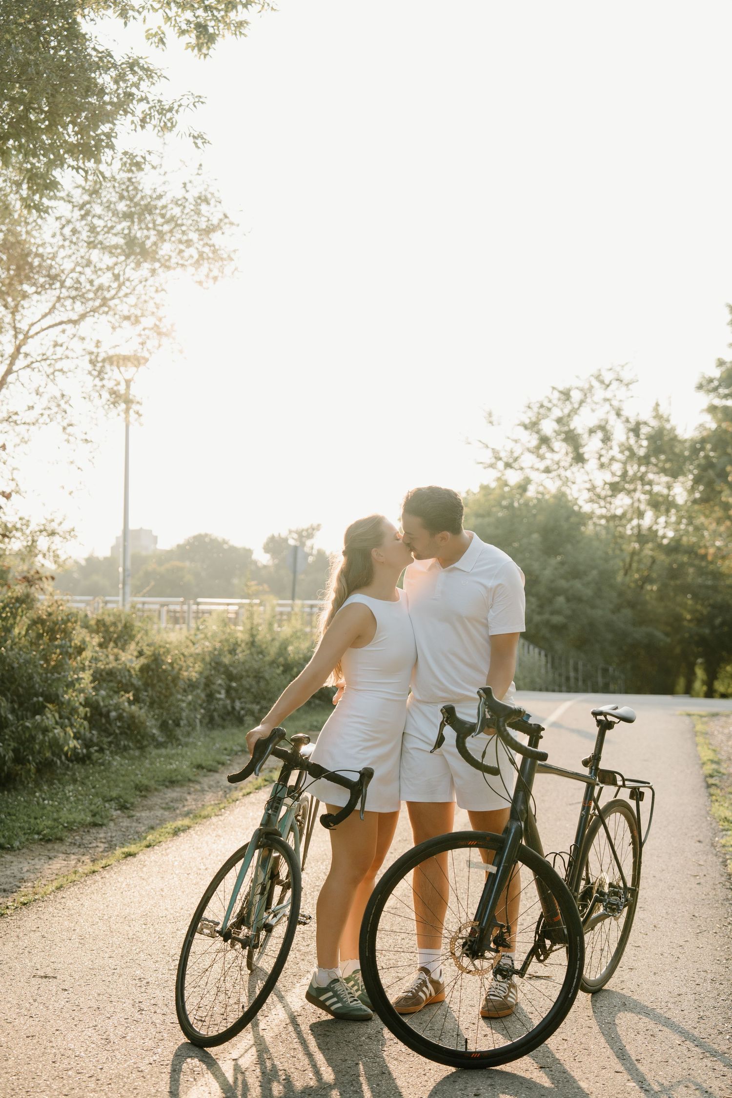Couple share a romantic moment on a sunny path while standing with their bicycles during golden hour.